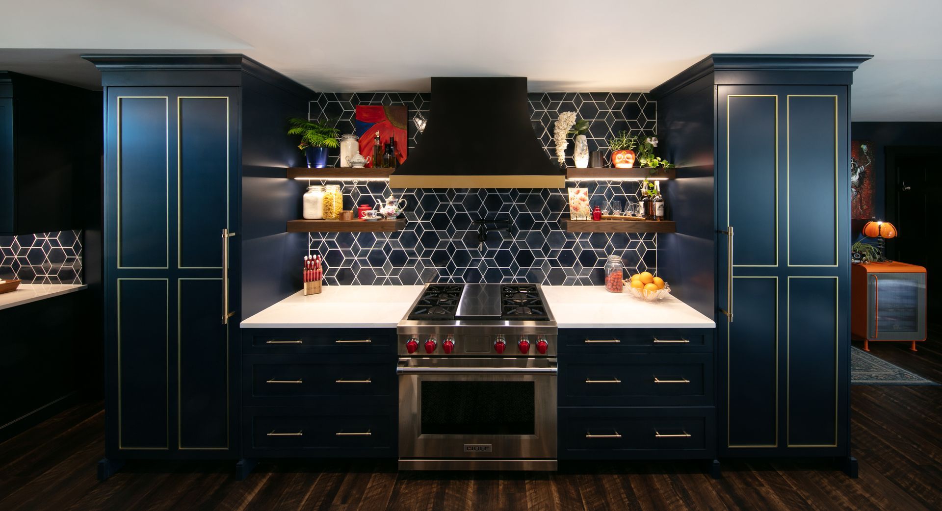 Navy blue kitchen with stainless steel appliances, hexagonal backsplash, and open shelving.
