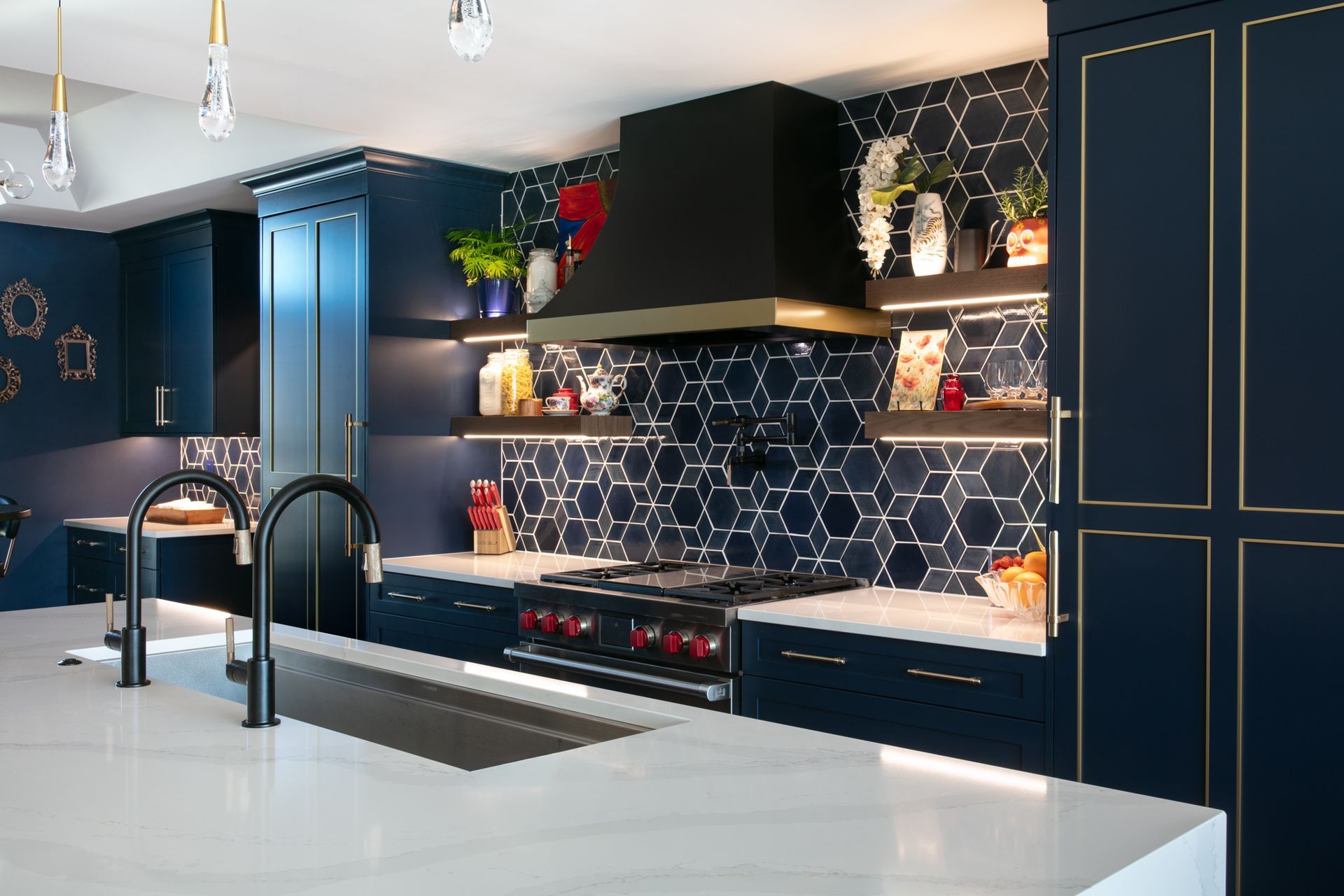 Navy blue kitchen with gold trim, white countertops, hexagon tile backsplash, and black range hood.