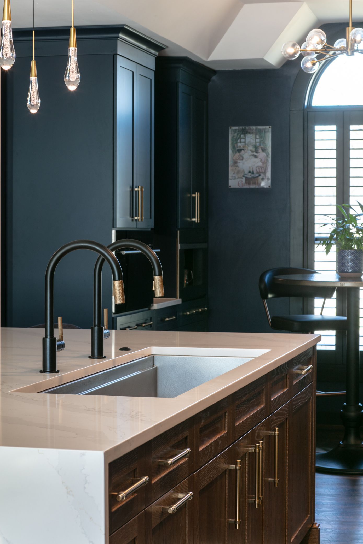 Dark blue kitchen with black faucet, gold hardware, and marble countertop.