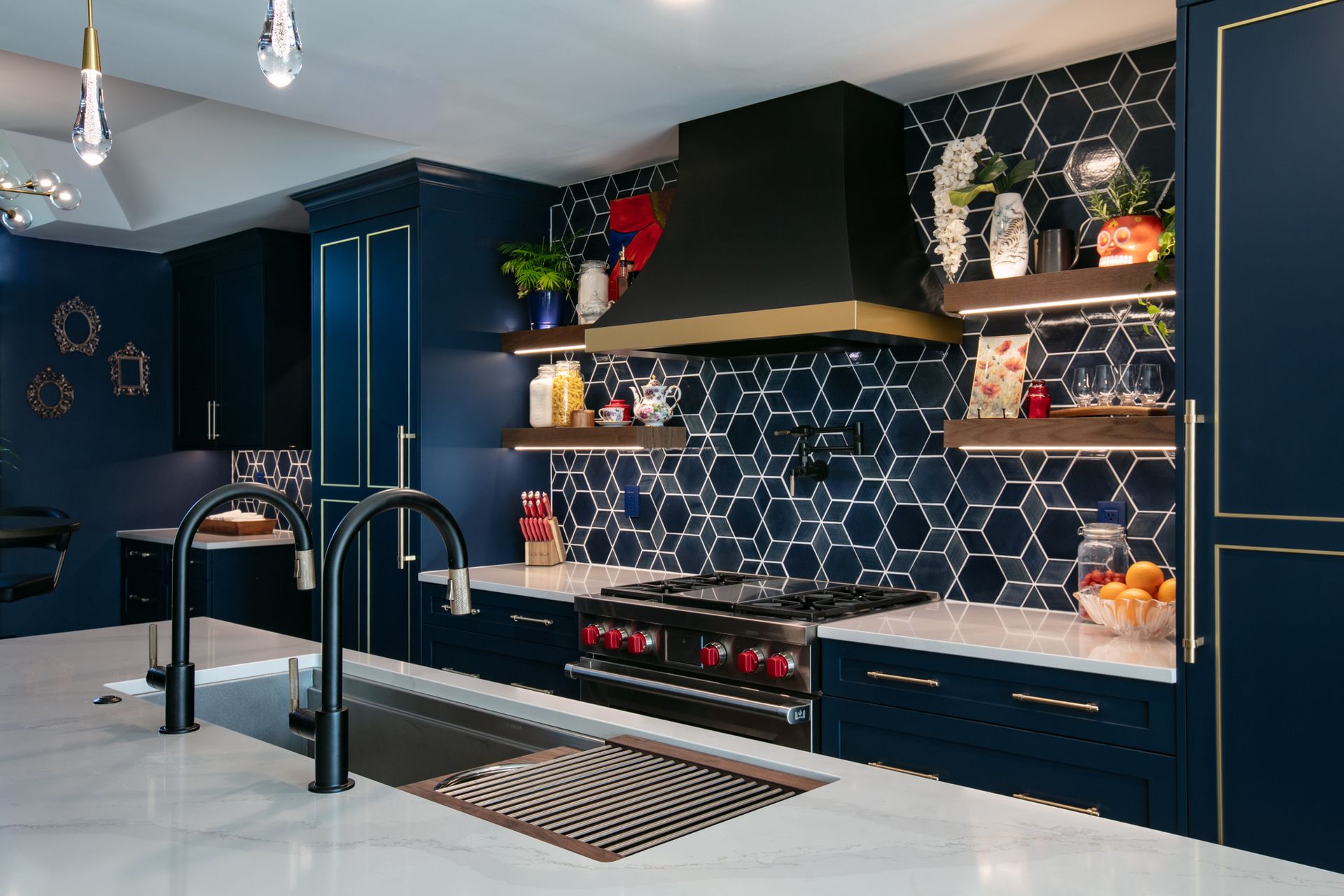Navy blue kitchen with white countertops, gold accents, hexagon tile backsplash, and stainless steel appliances.