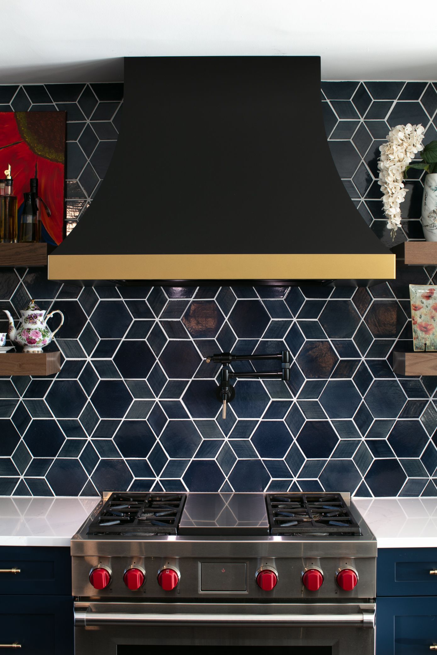 Modern kitchen with black range hood and blue geometric tile backsplash. Stainless steel stove.