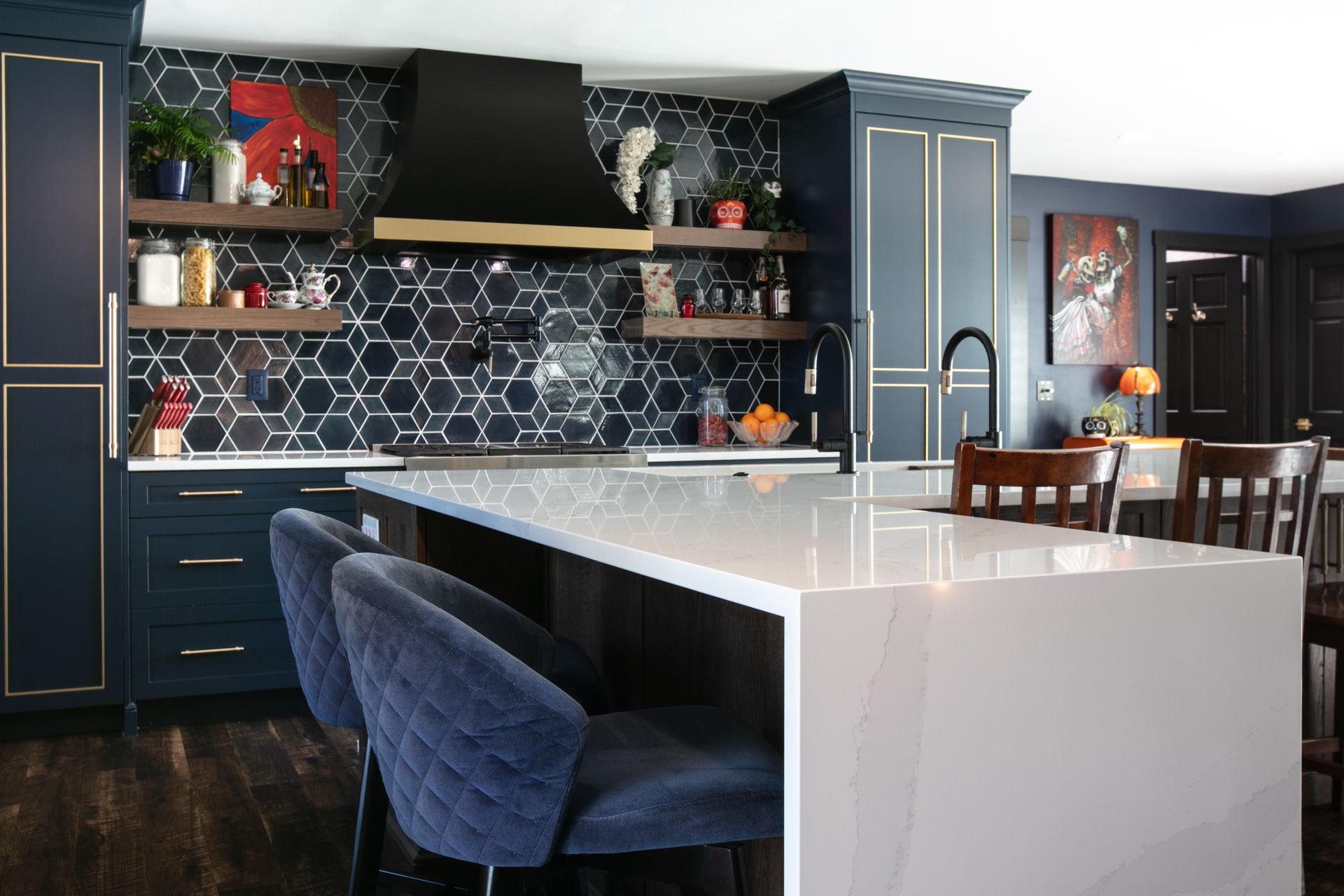 Dark blue kitchen with gold trim, white island, hexagon tile backsplash, and blue velvet bar stools.