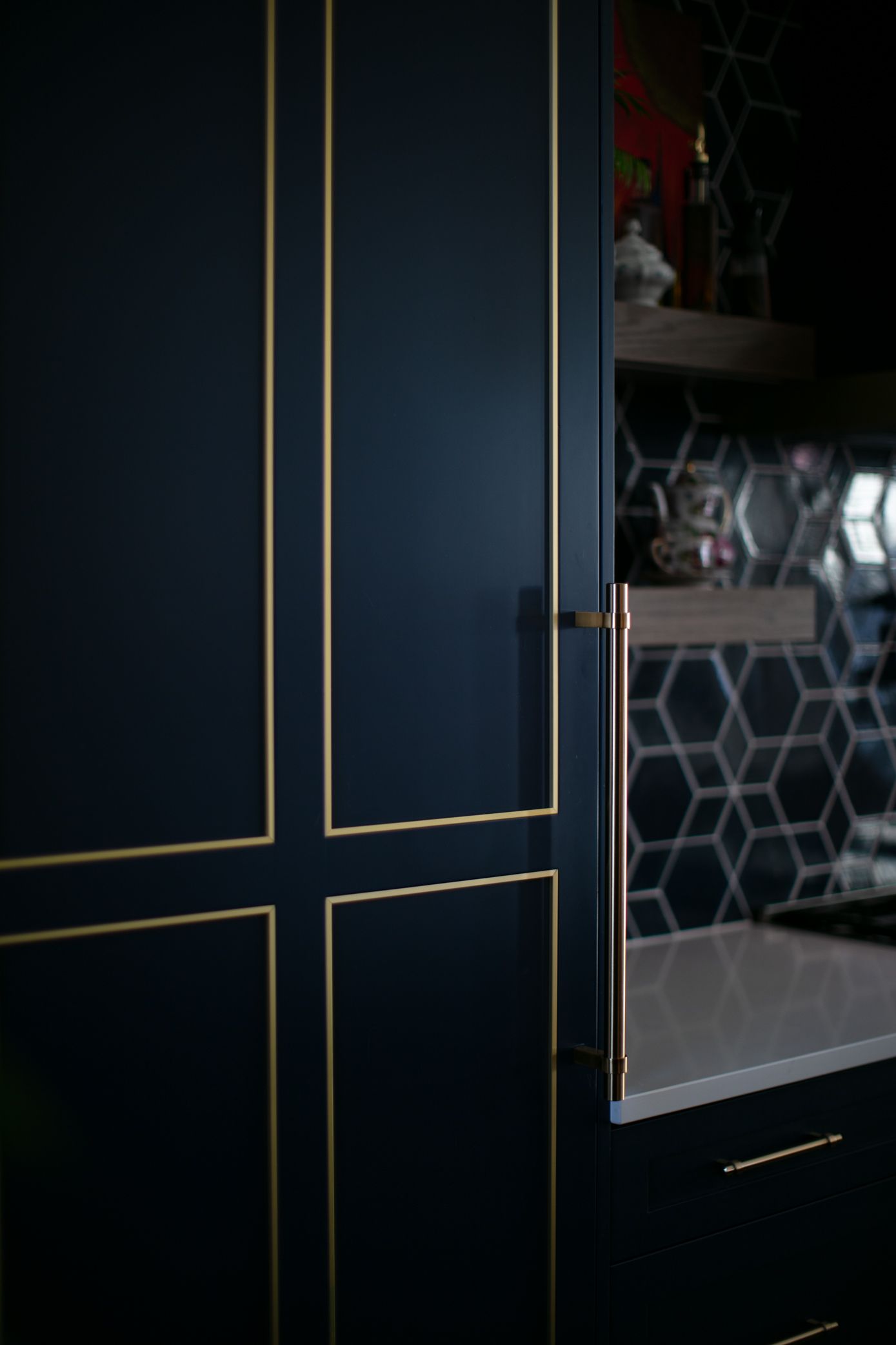 Dark blue cabinet with gold trim and copper handle, in a kitchen with hexagon tile backsplash.