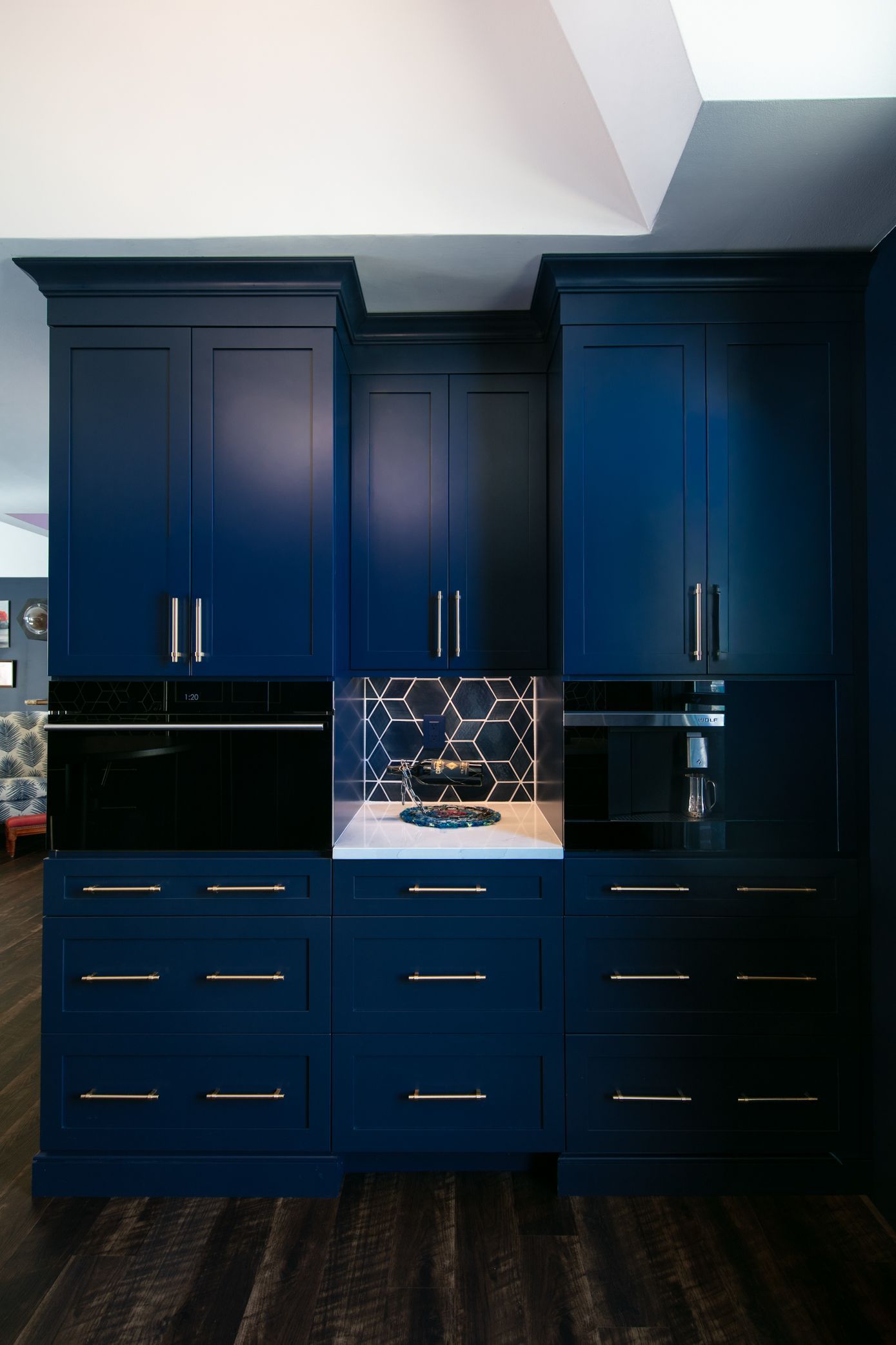 Navy blue cabinets with gold hardware and a glass display case in a room with dark wood floors.