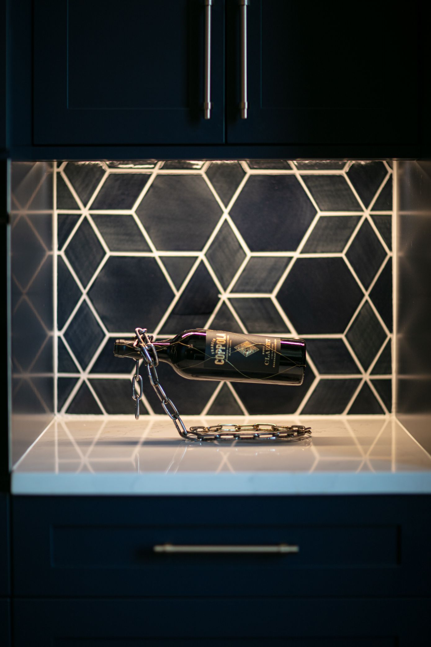 Dark kitchen cabinet with a wine bottle displayed on a metal holder against hexagonal patterned tile.