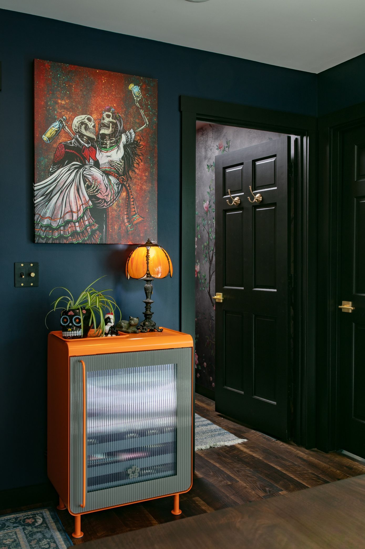 Orange cabinet with lamp and artwork in a dark blue room; black door and trim.