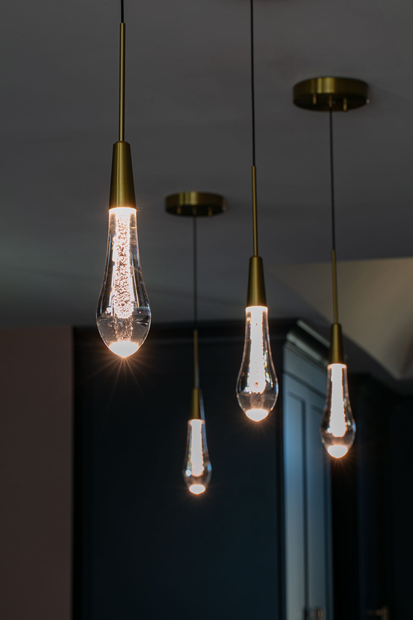Four teardrop-shaped pendant lights with gold hardware, illuminating a room with a dark wall.