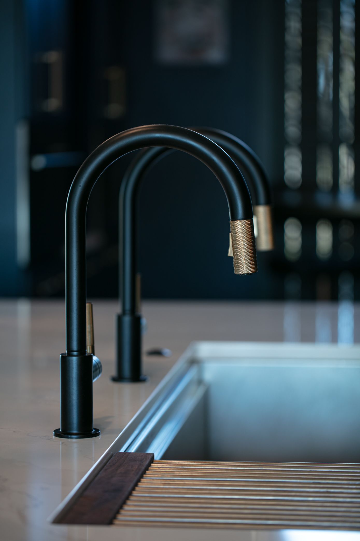 Black kitchen faucets with gold tips over a stainless steel sink.