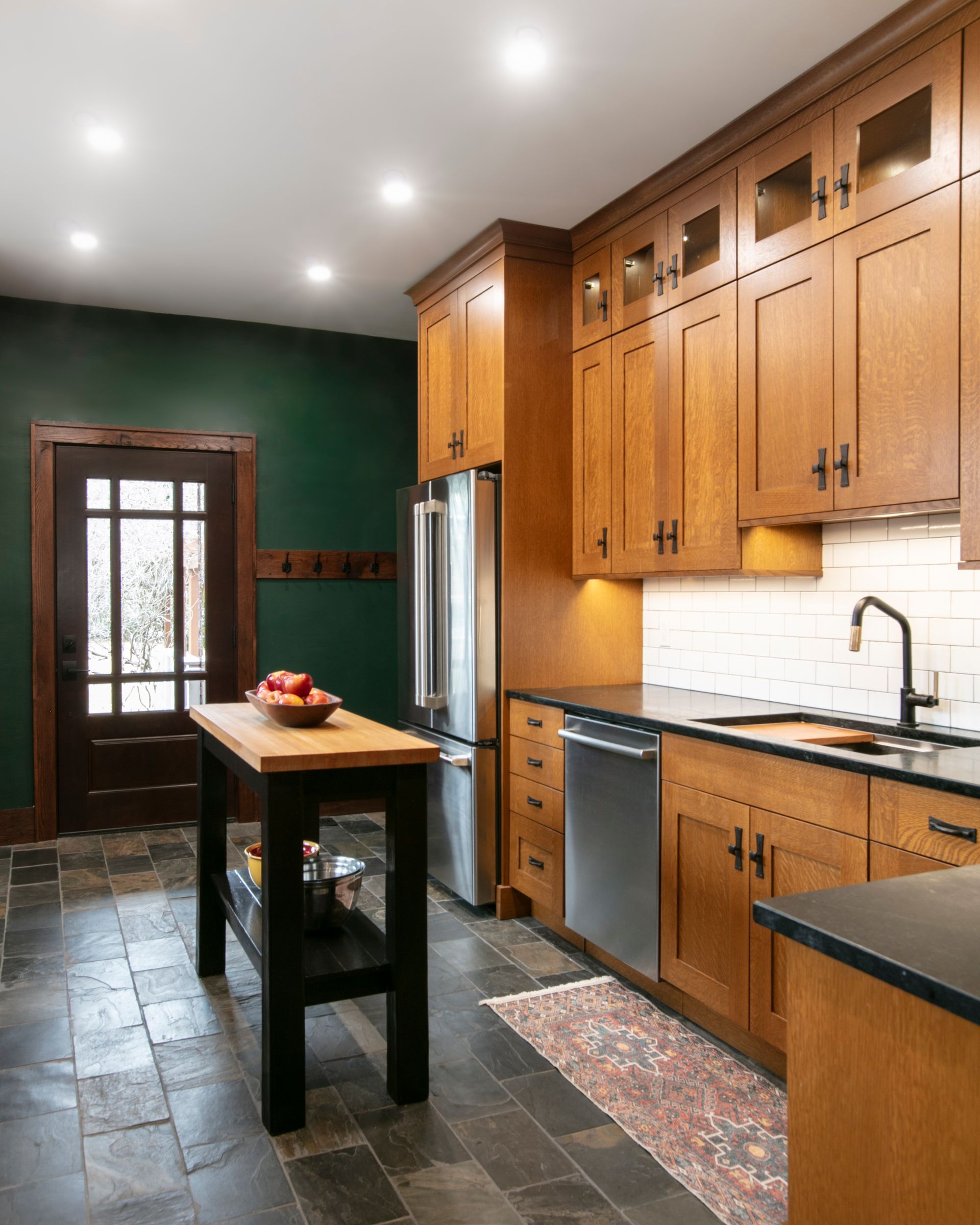 Kitchen with wooden cabinets, stainless steel appliances, and a black countertop island. Green wall, dark floor.