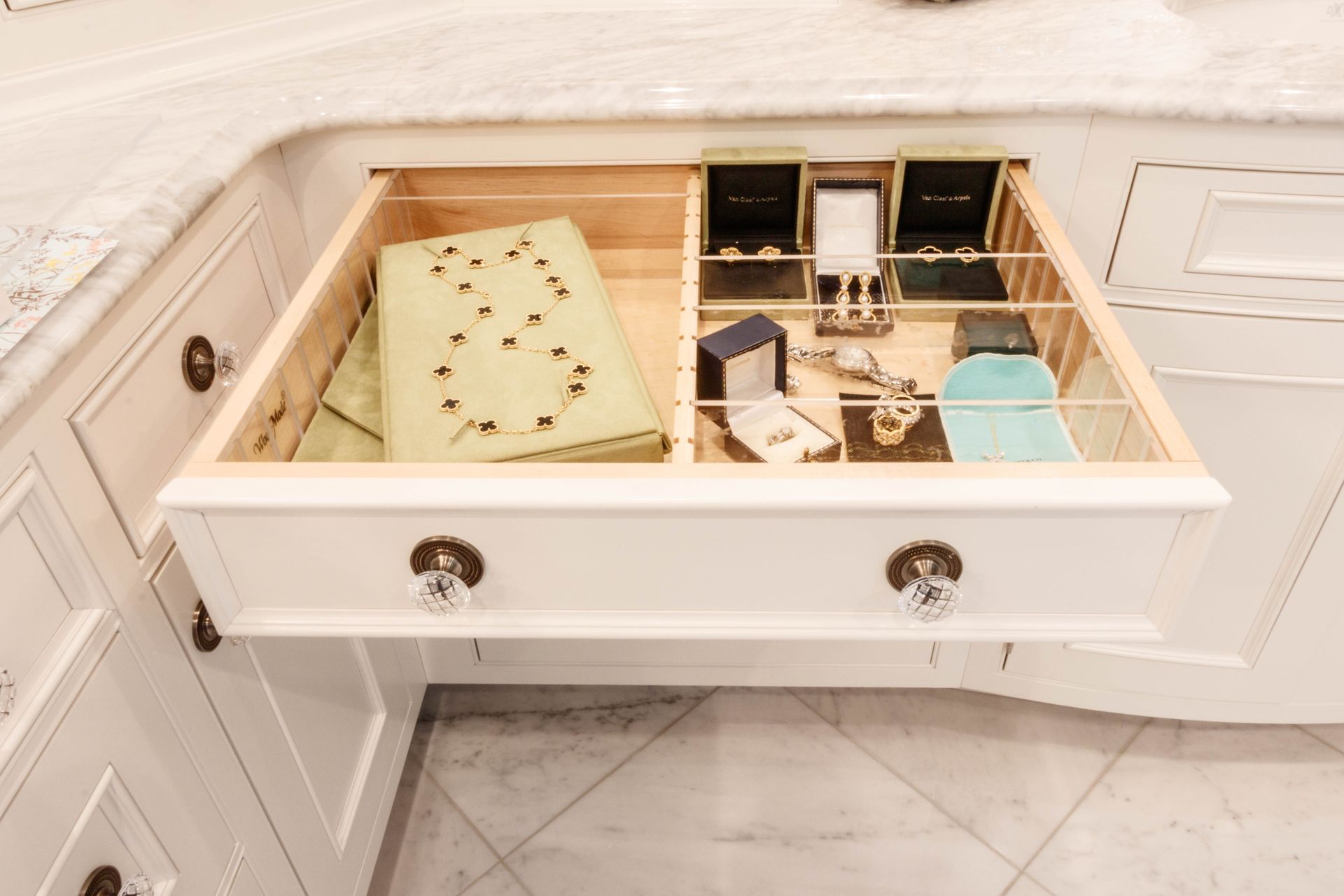 Open white kitchen drawer holding jewelry and ring boxes.