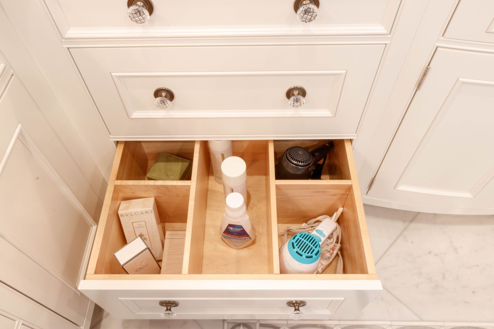 Open bathroom drawer with wooden dividers holding toiletries and hair care products.