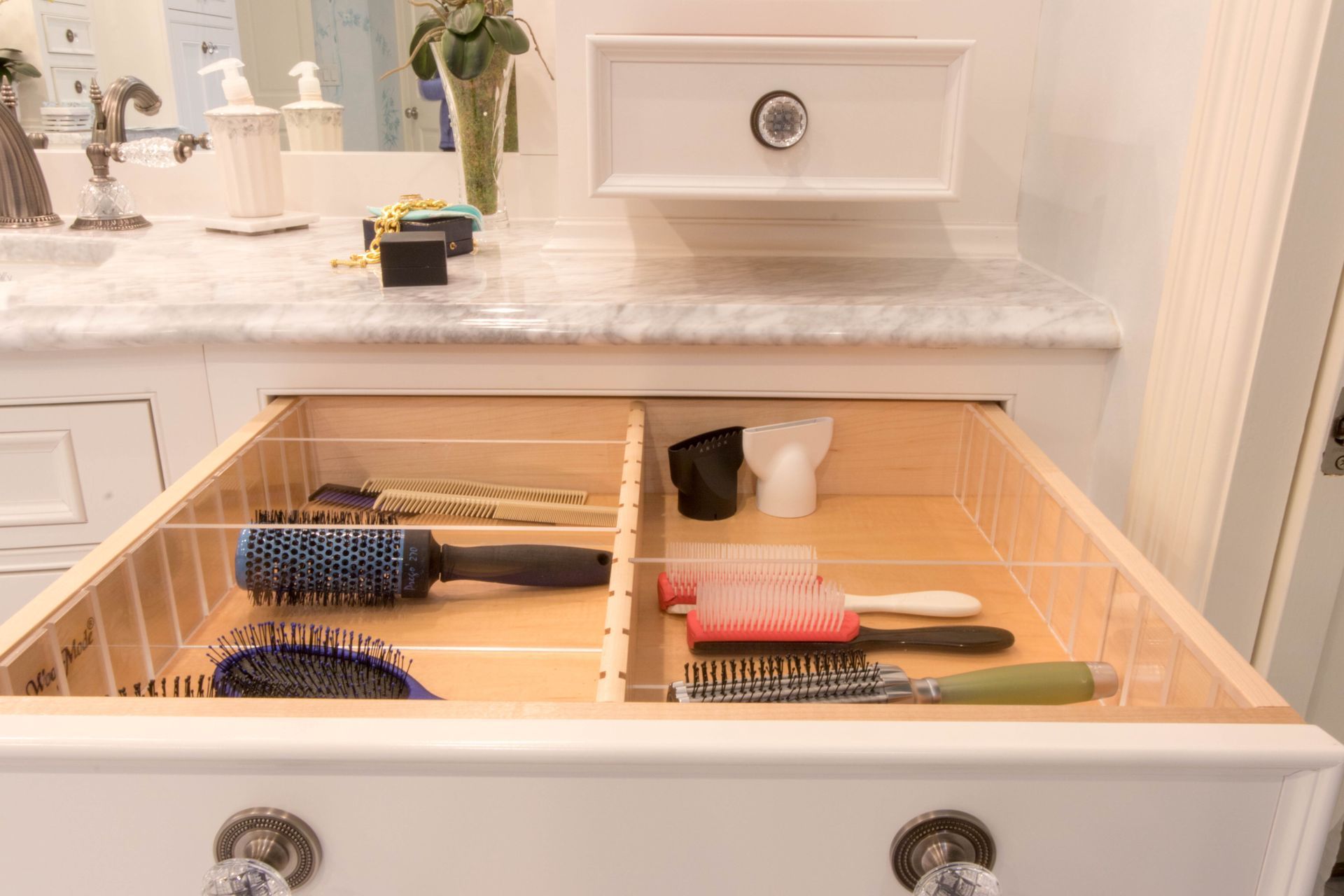 Open white bathroom drawer with hairbrushes separated by dividers.