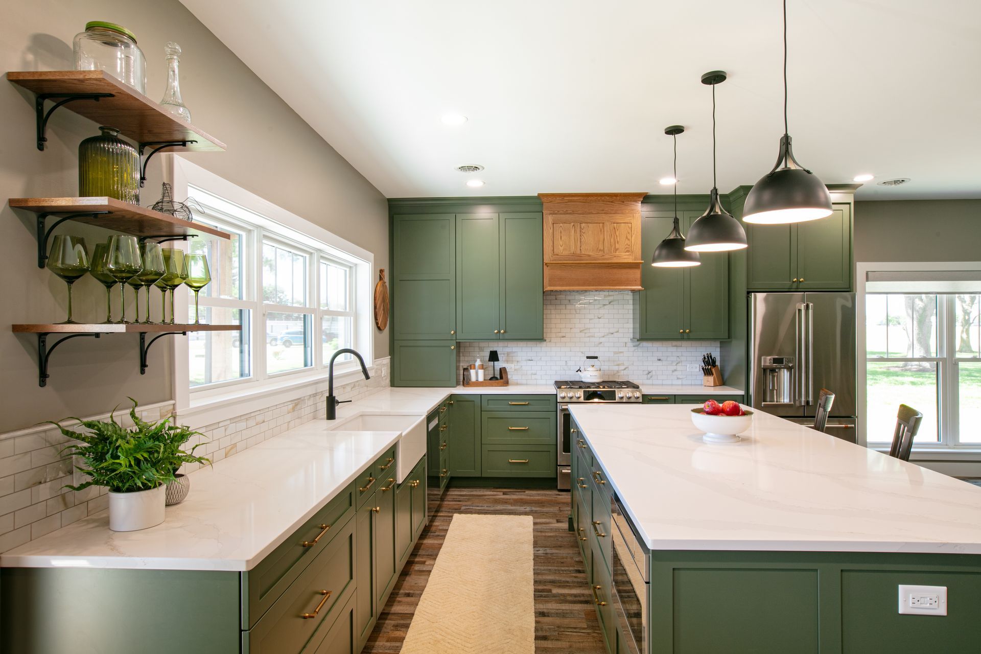 Green kitchen with white countertops, open shelving, and island with pendant lights.