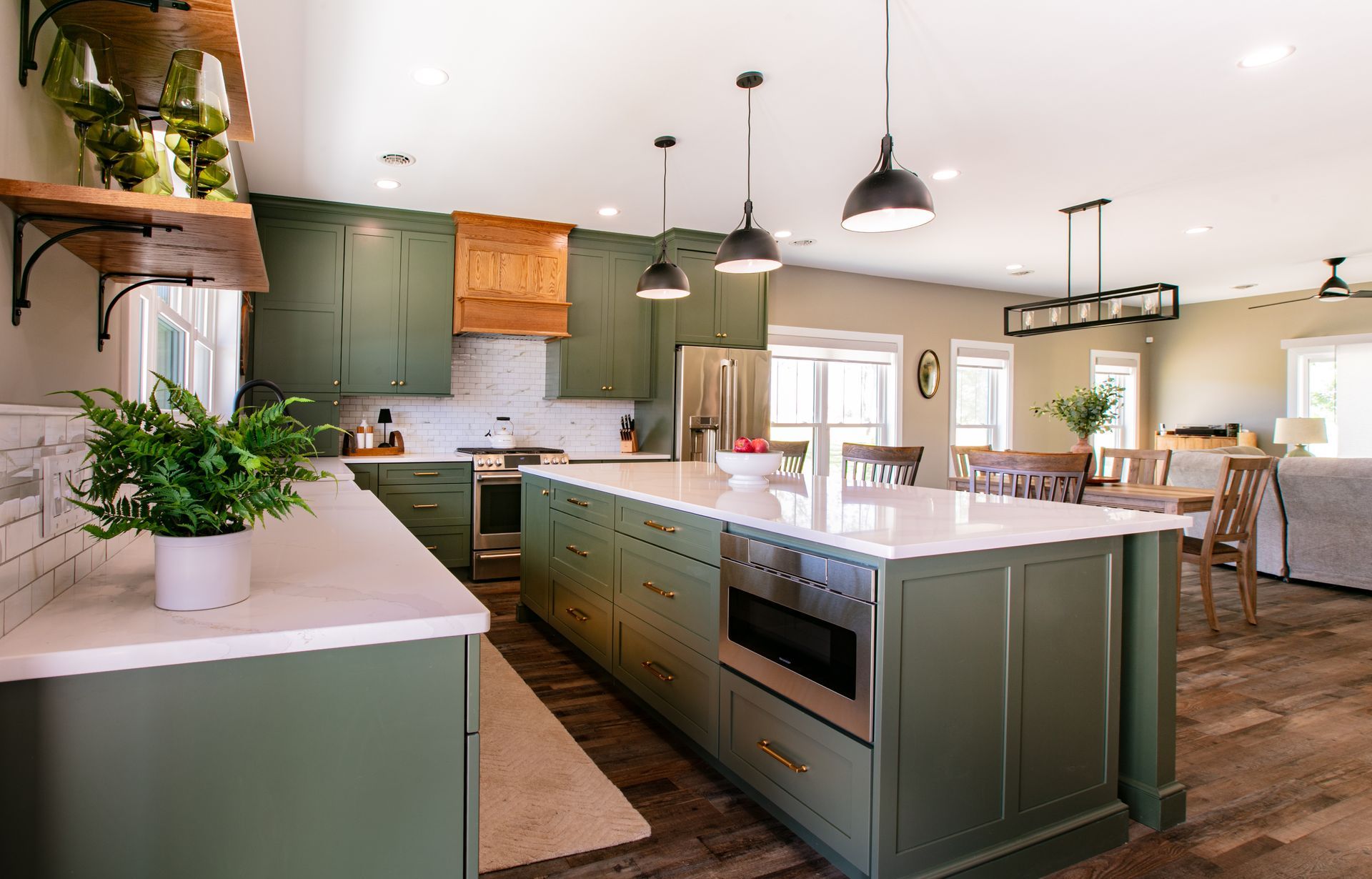 Green kitchen with white countertops, island, and wood accents. Dining area visible.