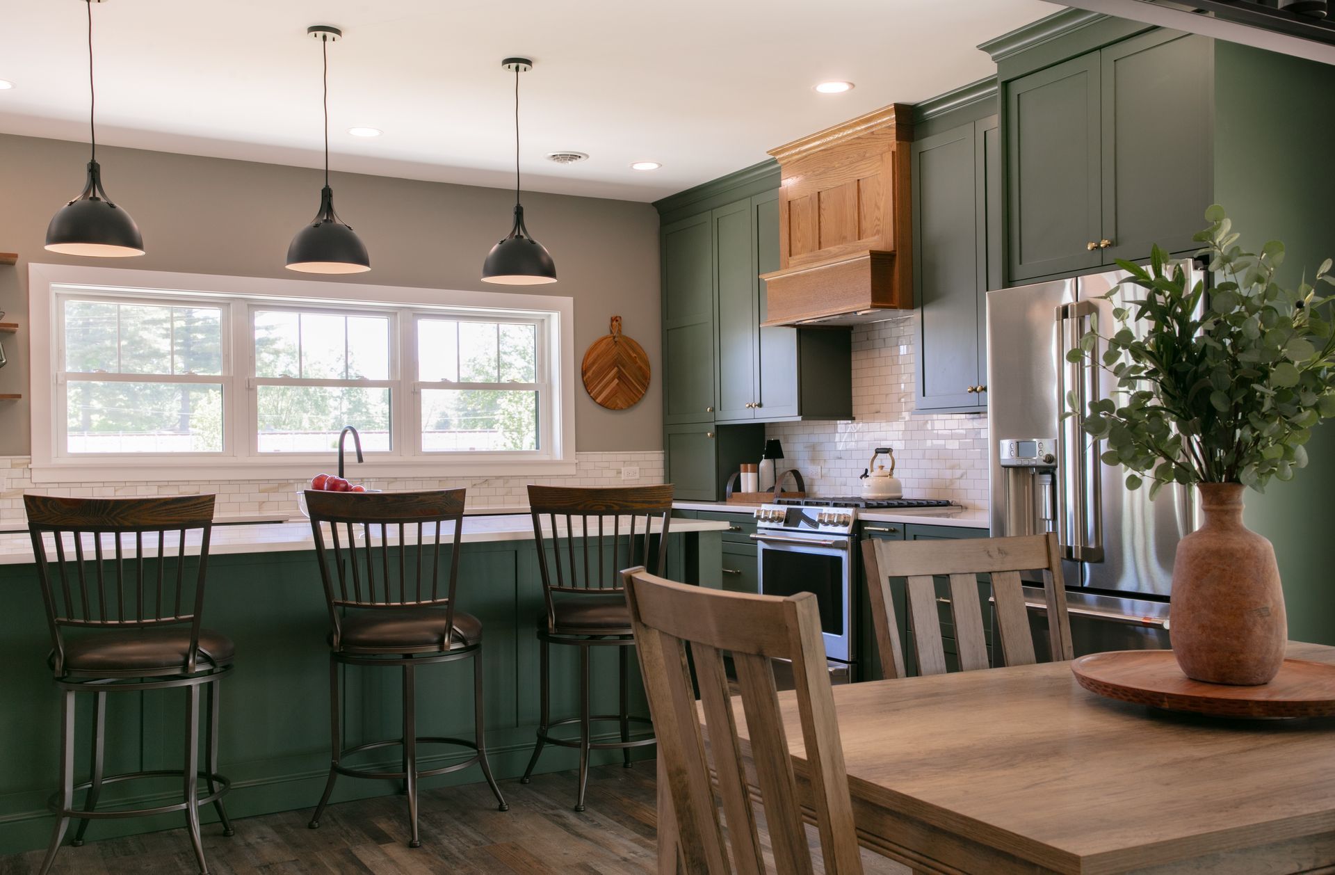 Green kitchen with island seating, stove, and dining table.