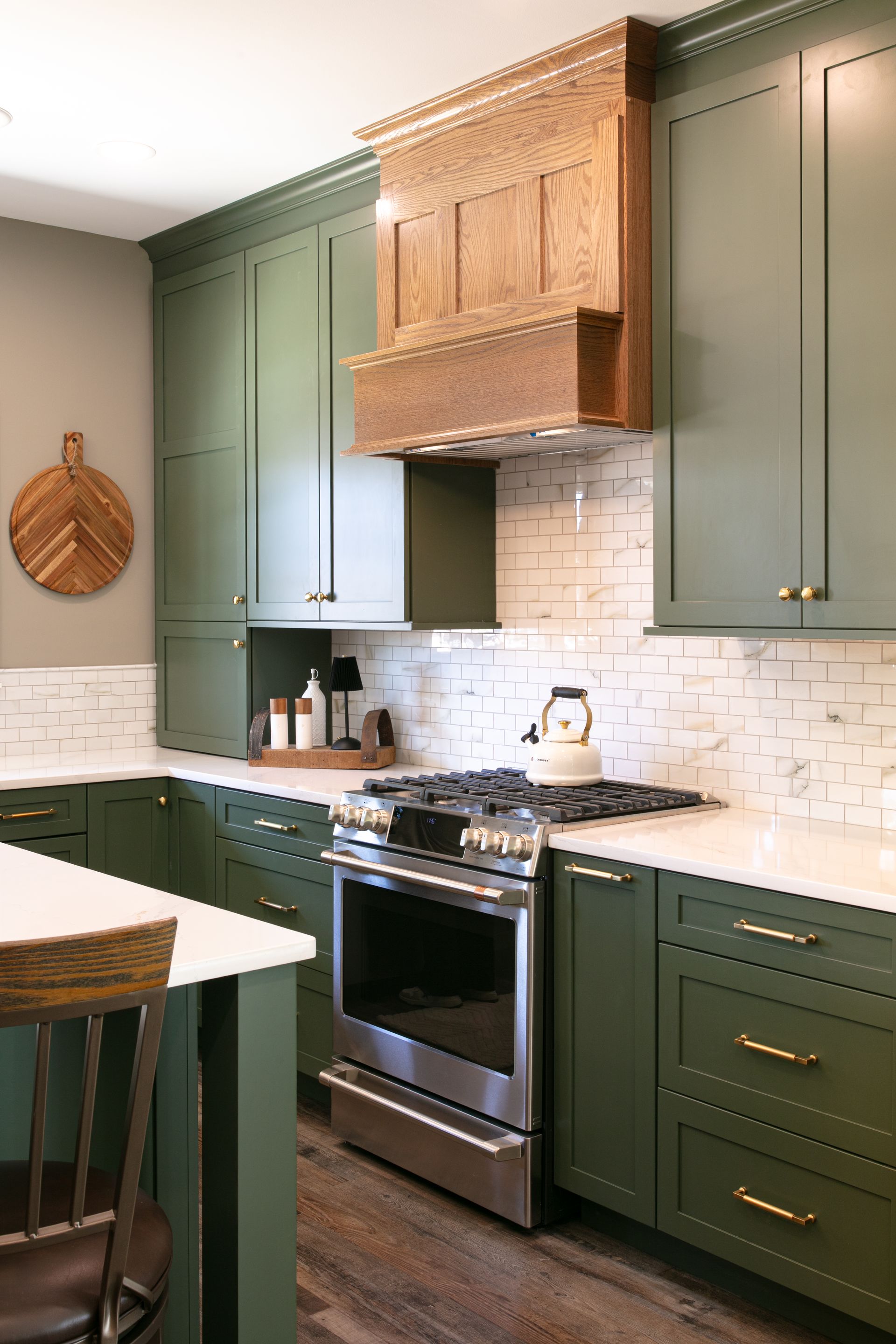 Green kitchen with white countertops and wooden range hood.