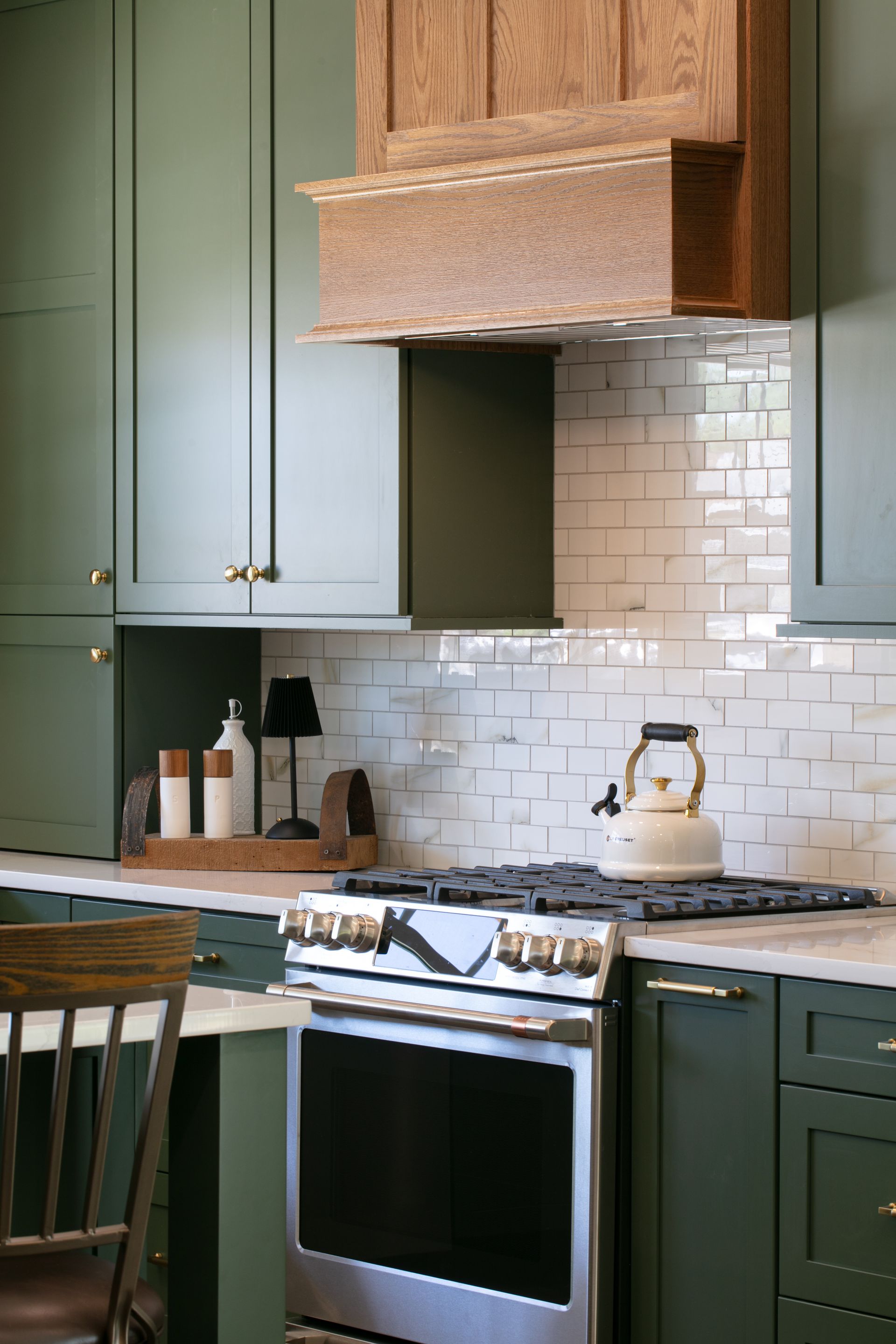 Green kitchen with wood range hood, white tile backsplash, and stainless steel oven.