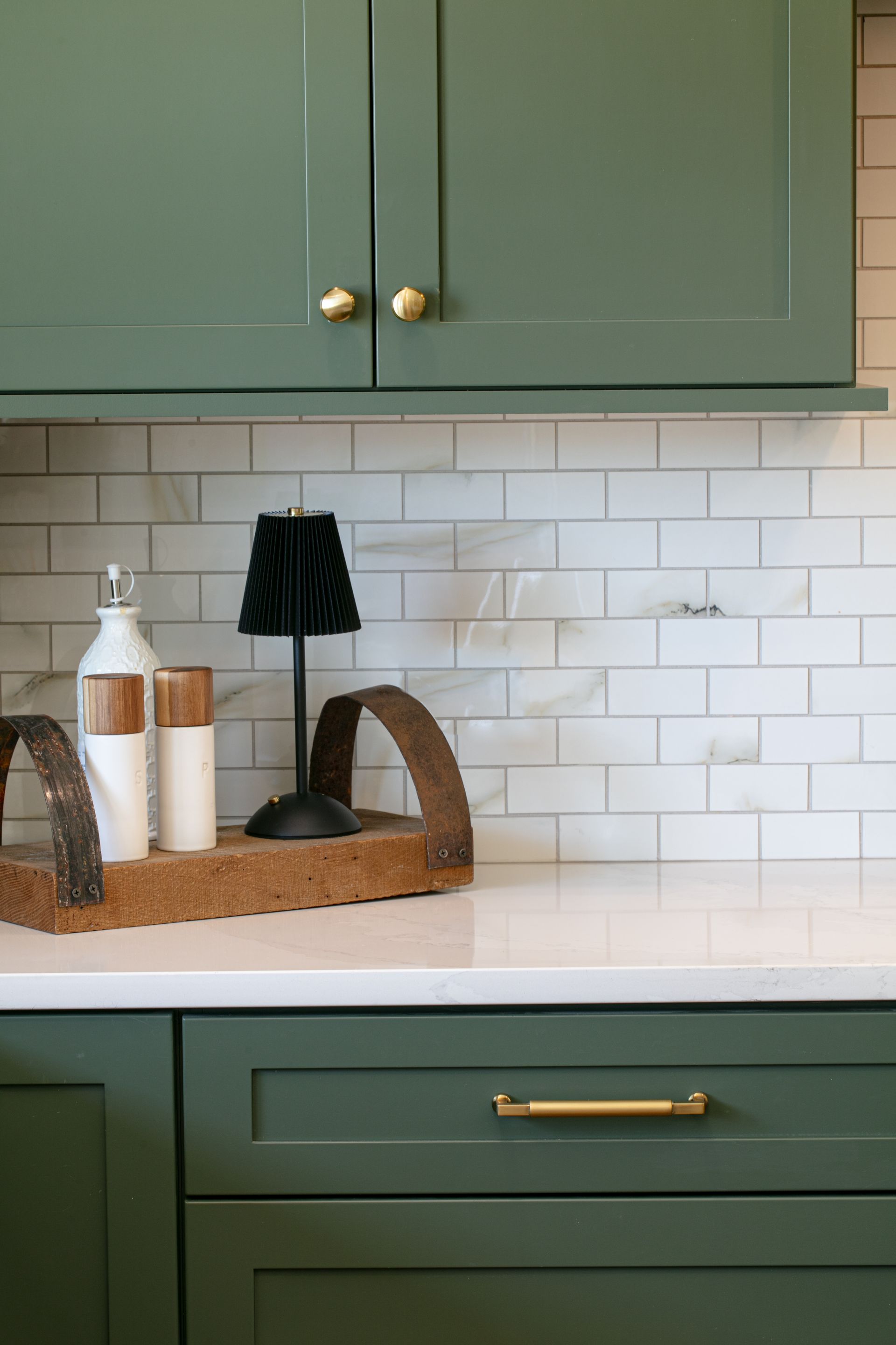 Green kitchen cabinets with gold hardware and white subway tile backsplash; decorative tray on countertop.