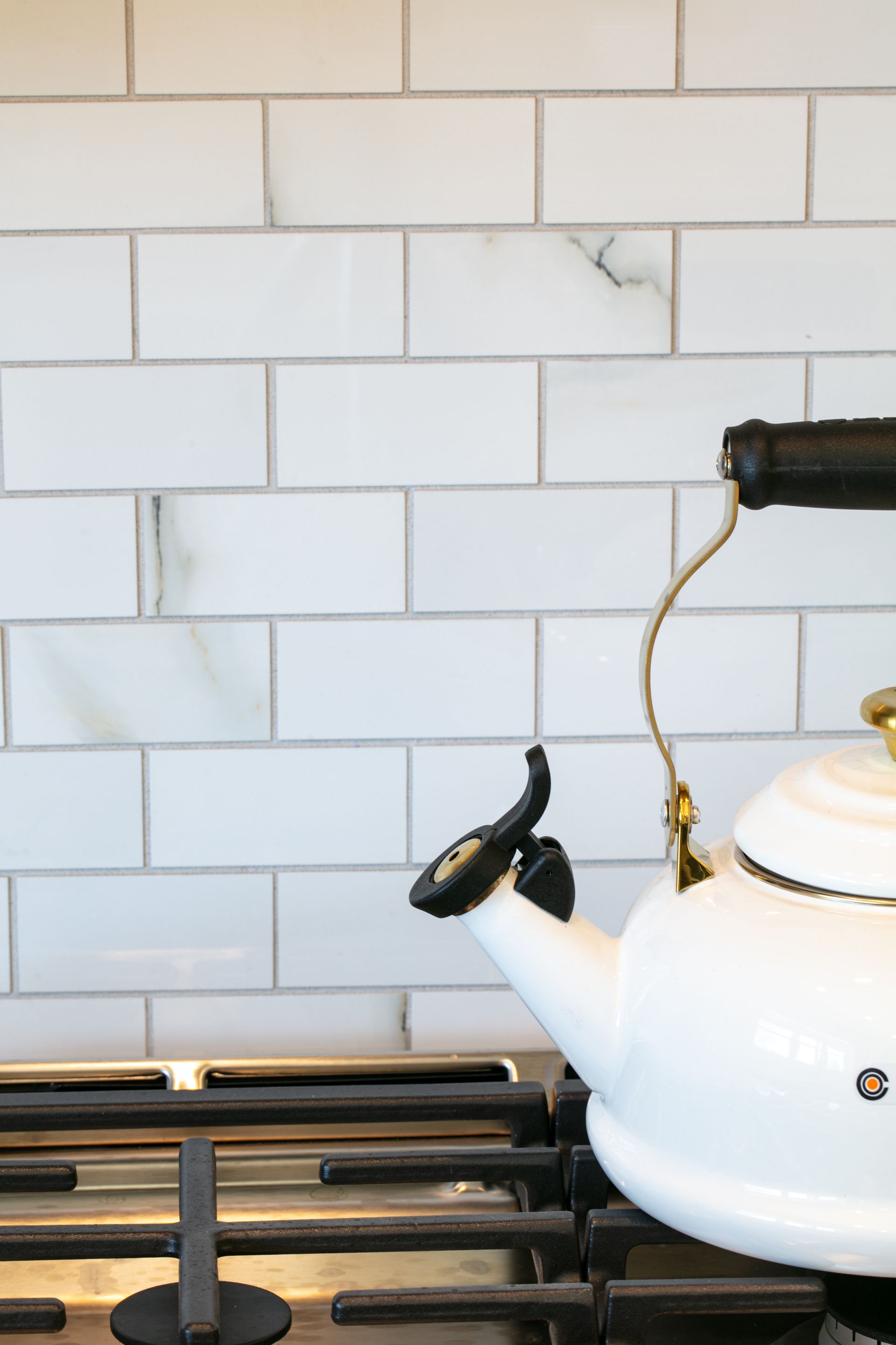 White tea kettle on a gas stove in front of white subway tile backsplash.