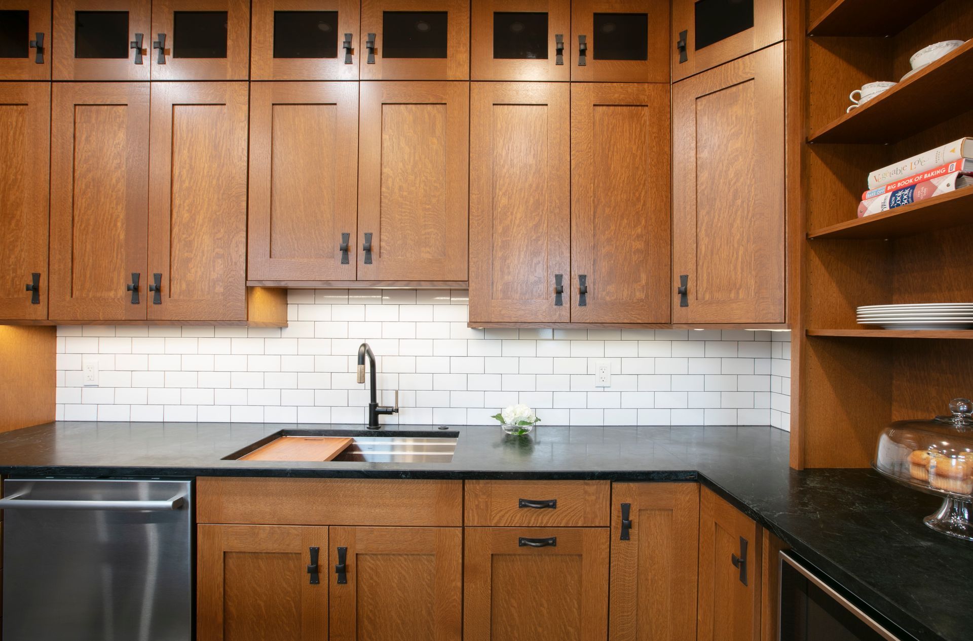 Wooden kitchen cabinets with a black countertop and white tiled backsplash.