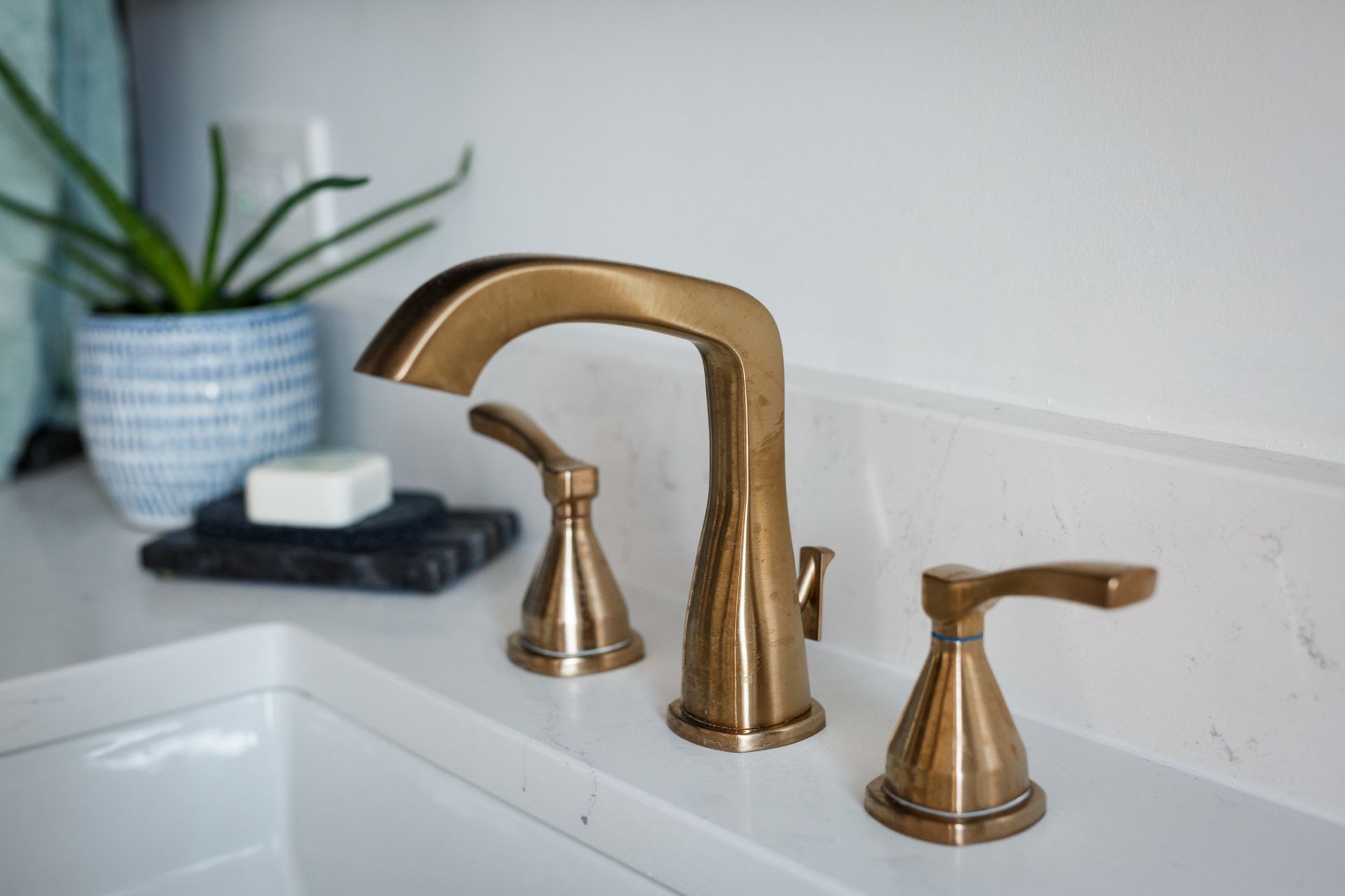Gold bathroom faucet with two levers and a curved spout on a white counter.