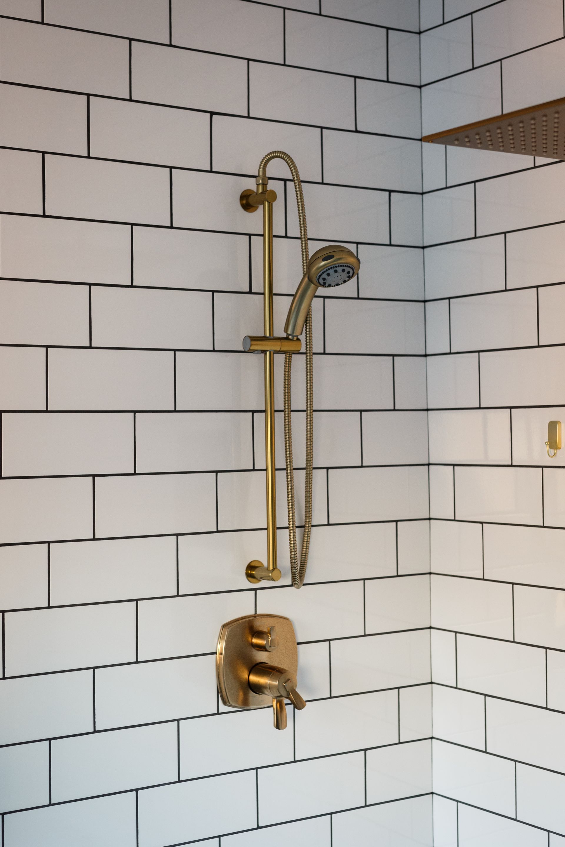 Gold shower fixtures against white subway tile in a bathroom corner.