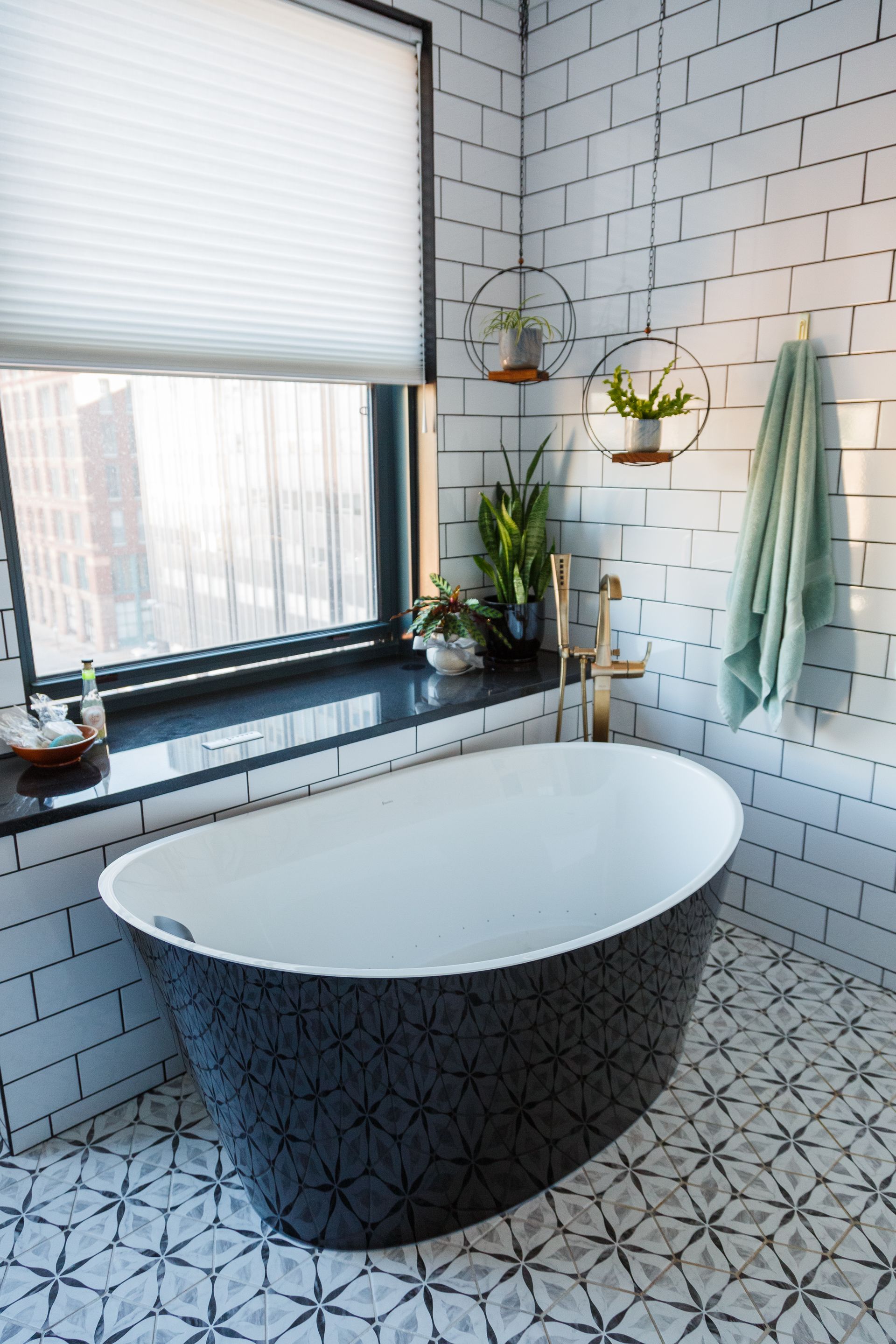 Bathroom with a black patterned tub, white brick-like tile, and a window with a blind.