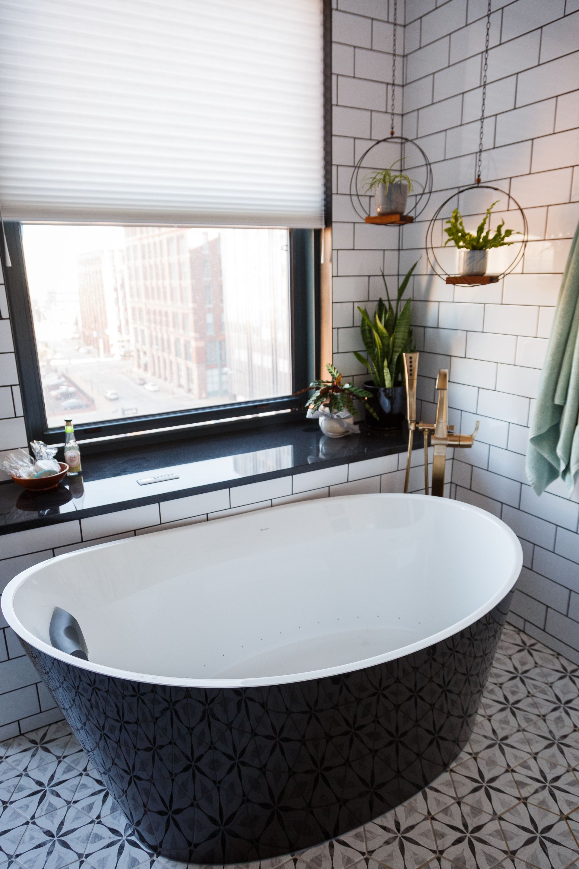 Stylish black and white patterned bathtub in a modern bathroom with a large window and hanging plants.