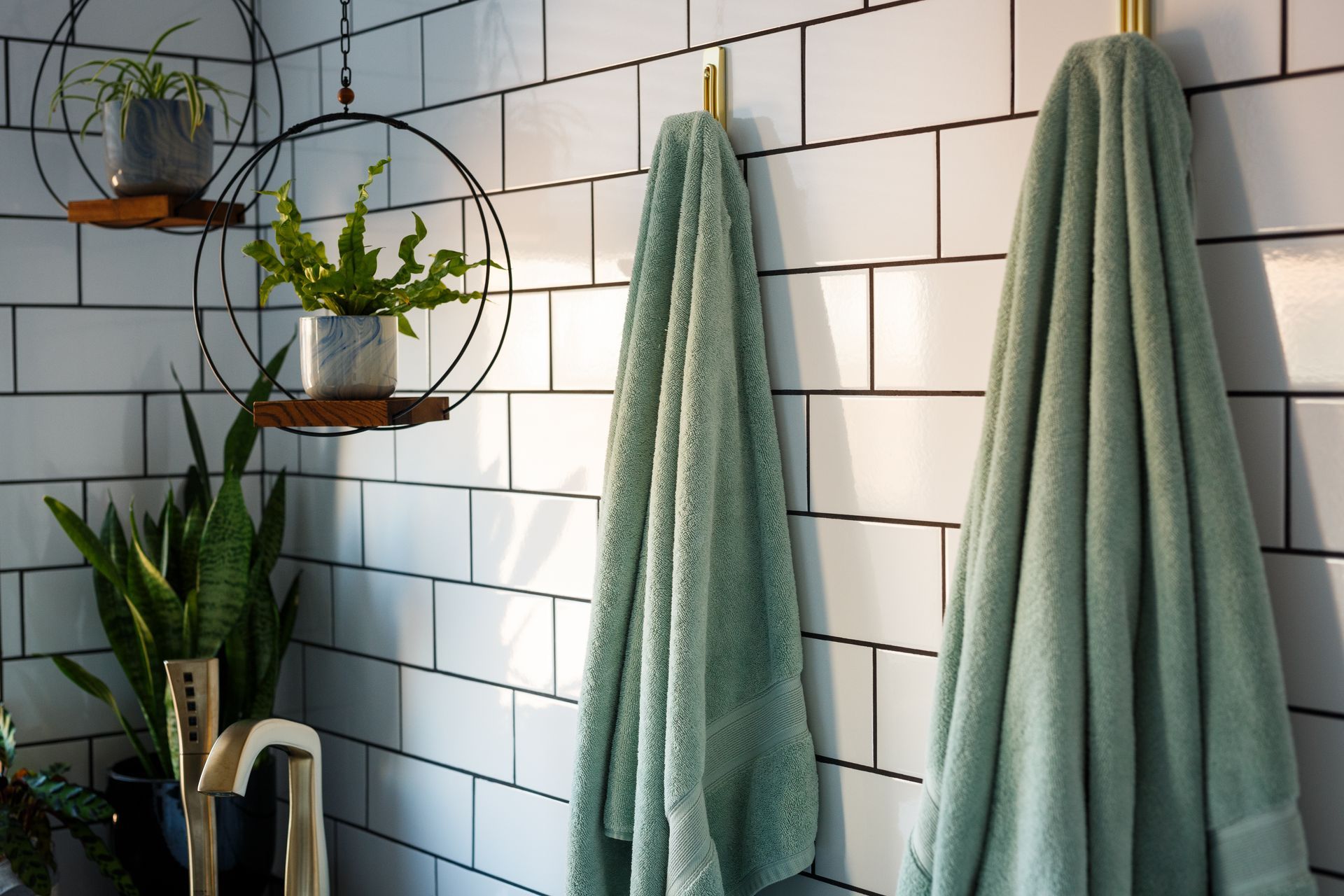 Bathroom with white subway tile, two green towels hanging, and plants.