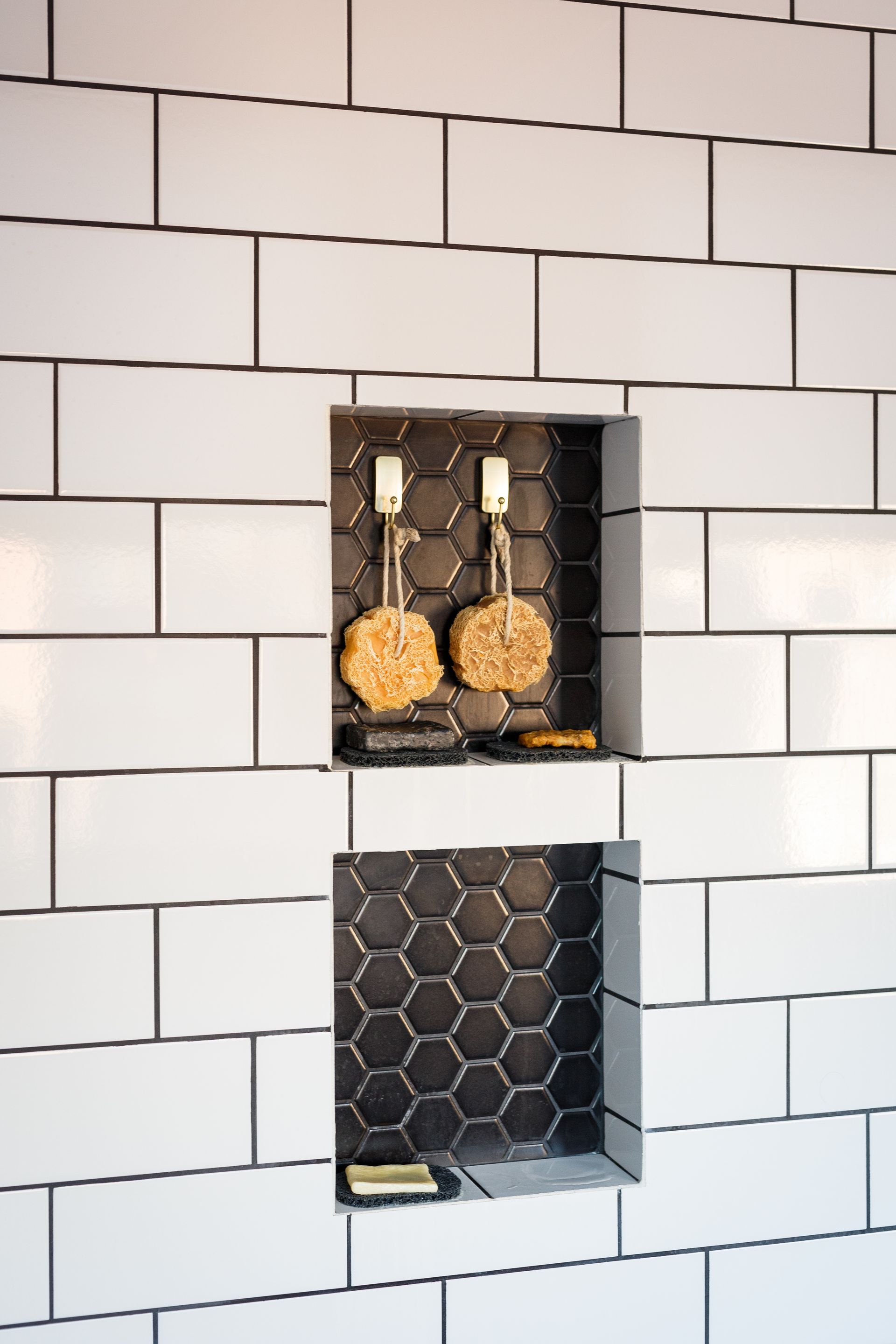 White subway tile wall with recessed niches. One niche has loofahs hanging; the other is empty.