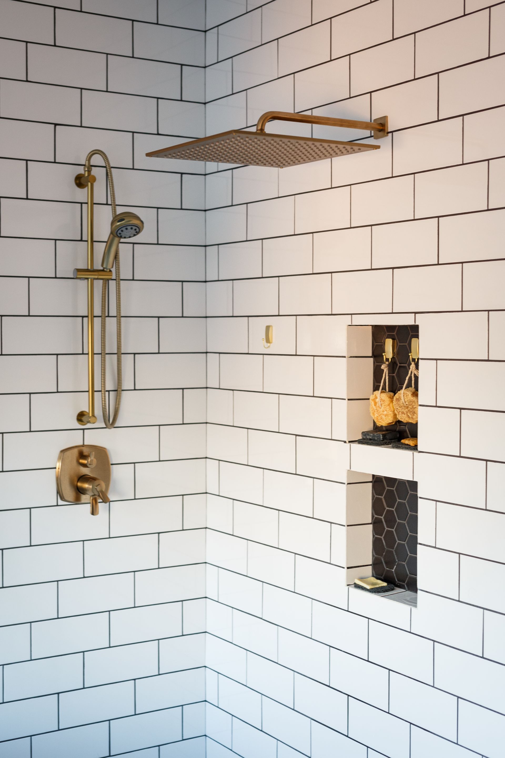 Gold fixtures in a shower with white subway tile. Built-in niche holds bottles.