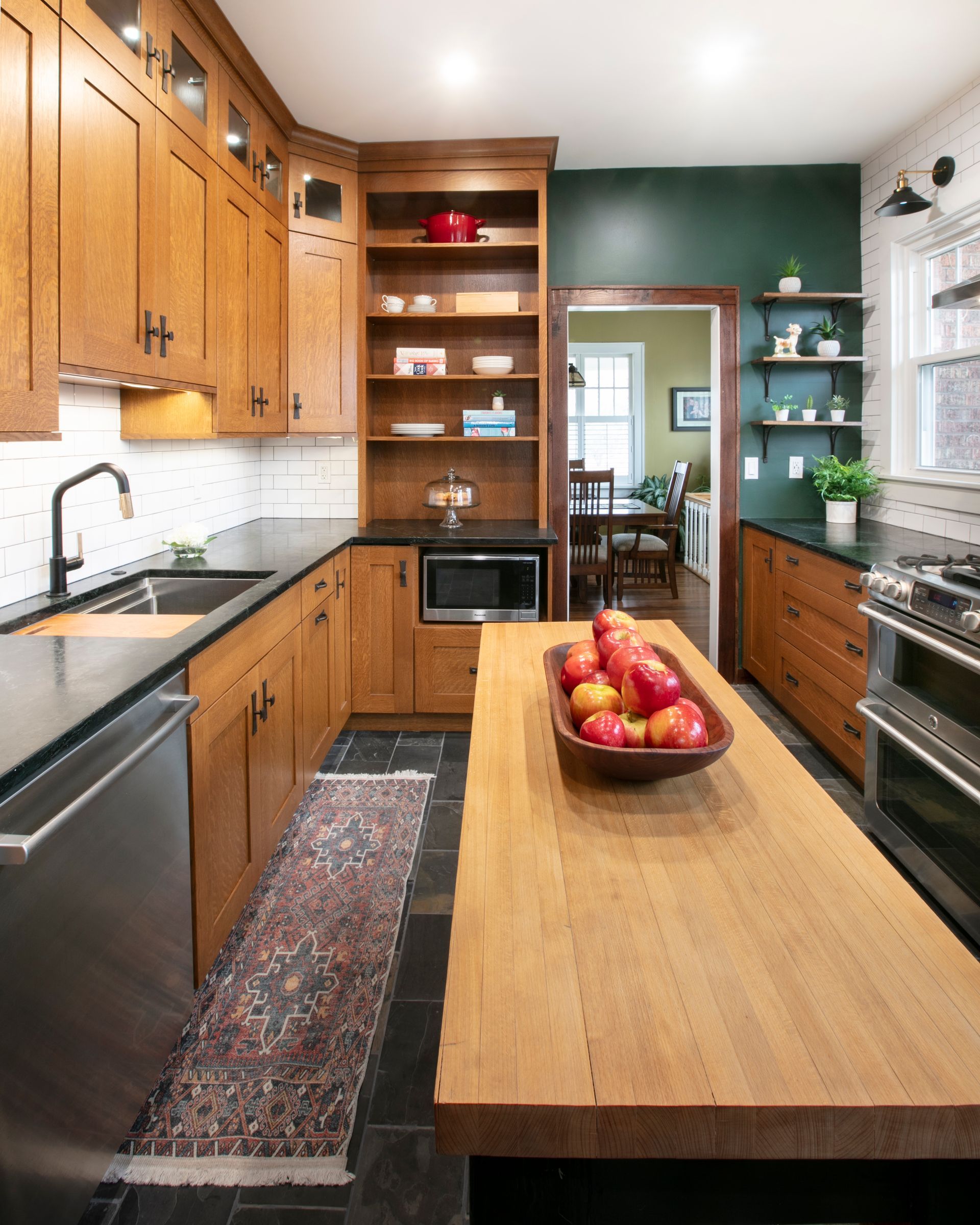 Cozy kitchen with wooden cabinets, black countertops, and a wooden island. Dark green accent wall and open doorway.