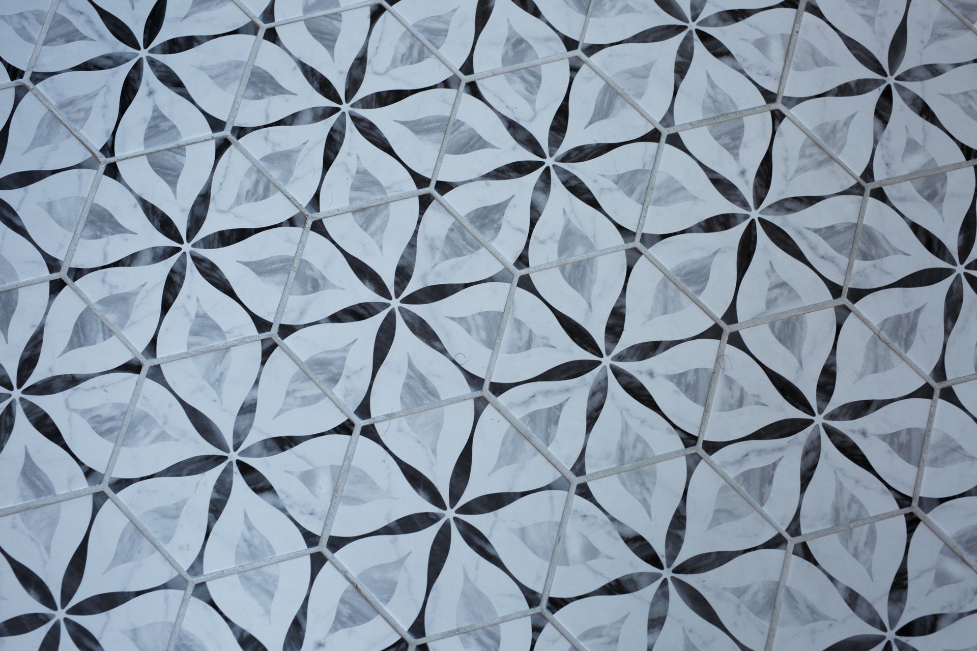 Abstract tiled floor pattern: repeating dark floral shapes within a light gray diamond grid.