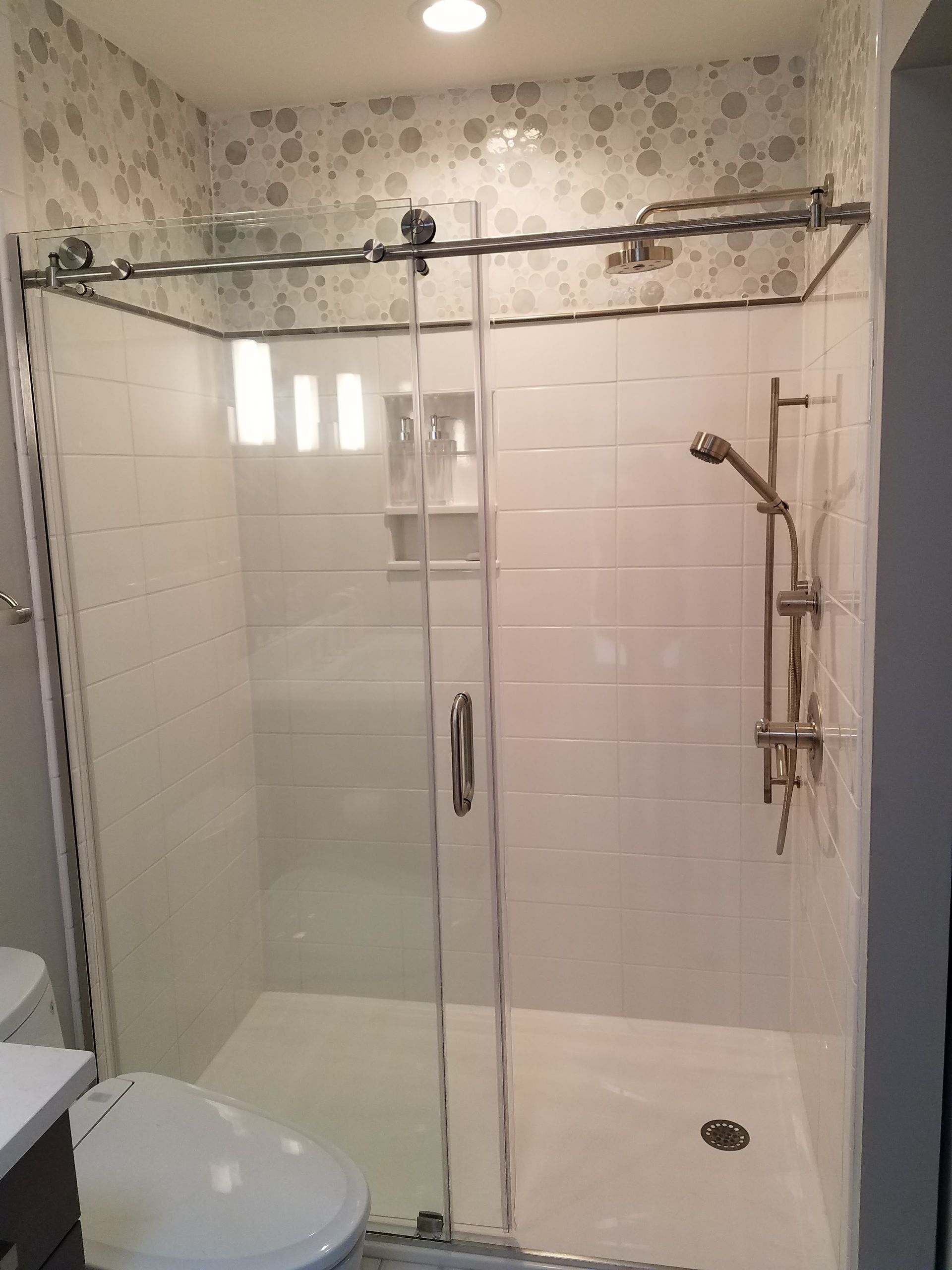 Modern bathroom with glass shower enclosure, white tiles, and chrome fixtures.