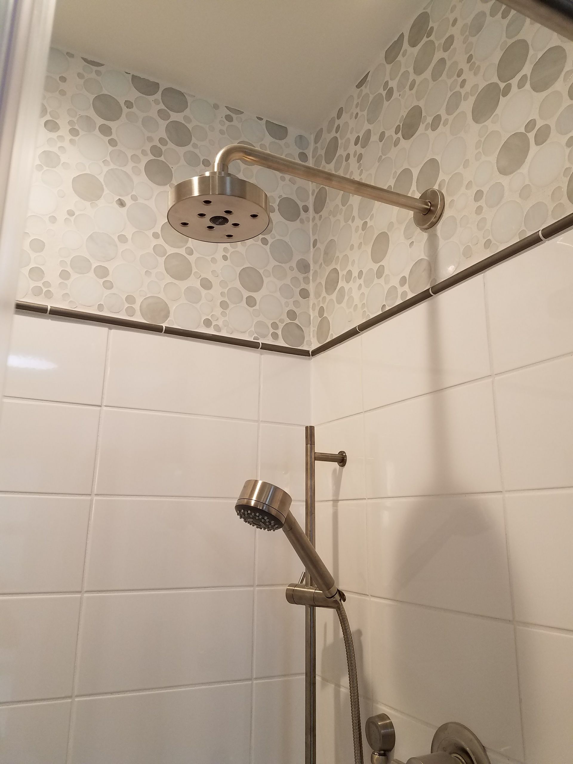 Shower with overhead and handheld showerheads, white and patterned tile walls, and a black accent border.