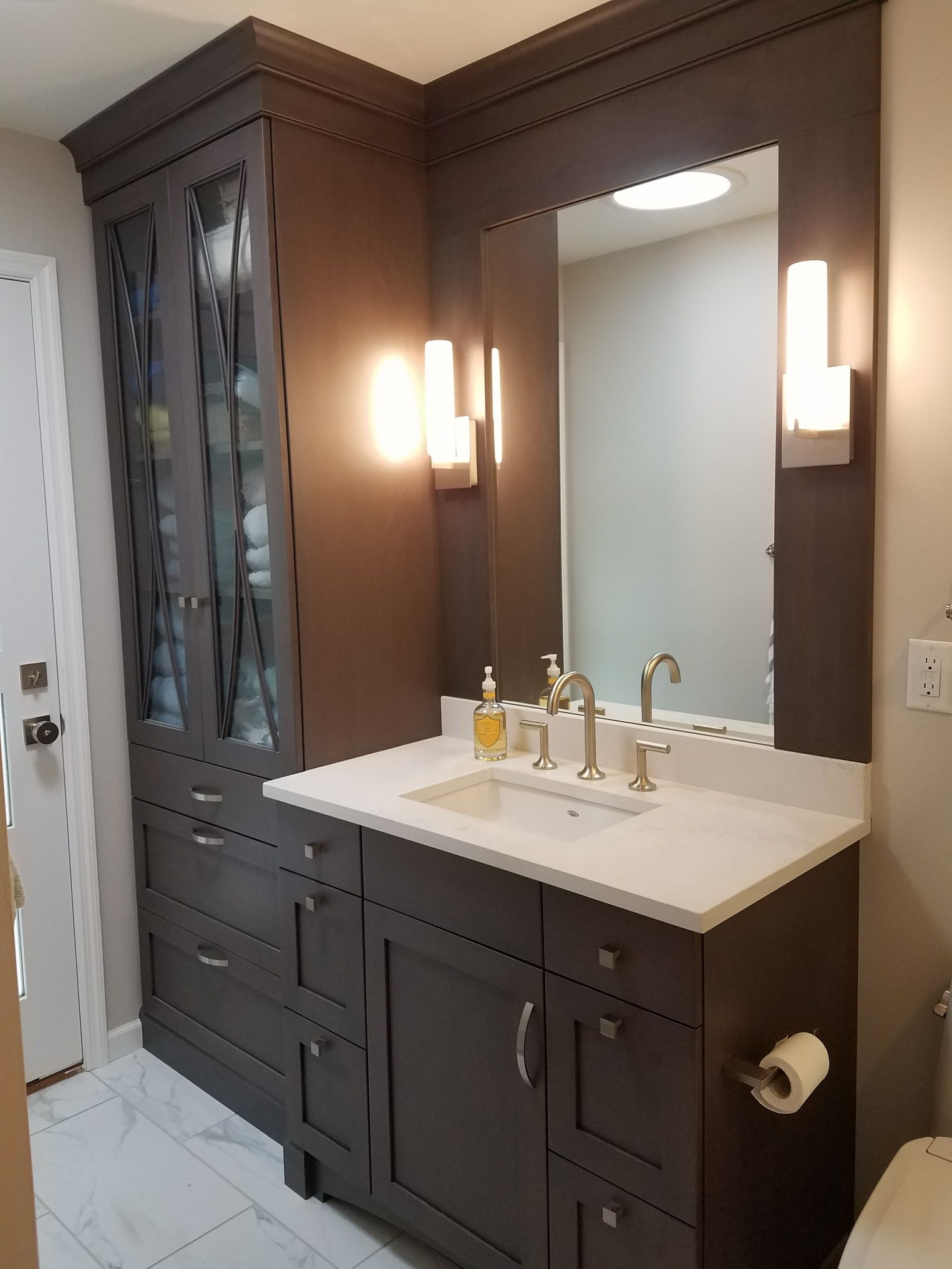 Dark gray bathroom vanity with mirror, cabinet, and white countertop. Modern sconces.