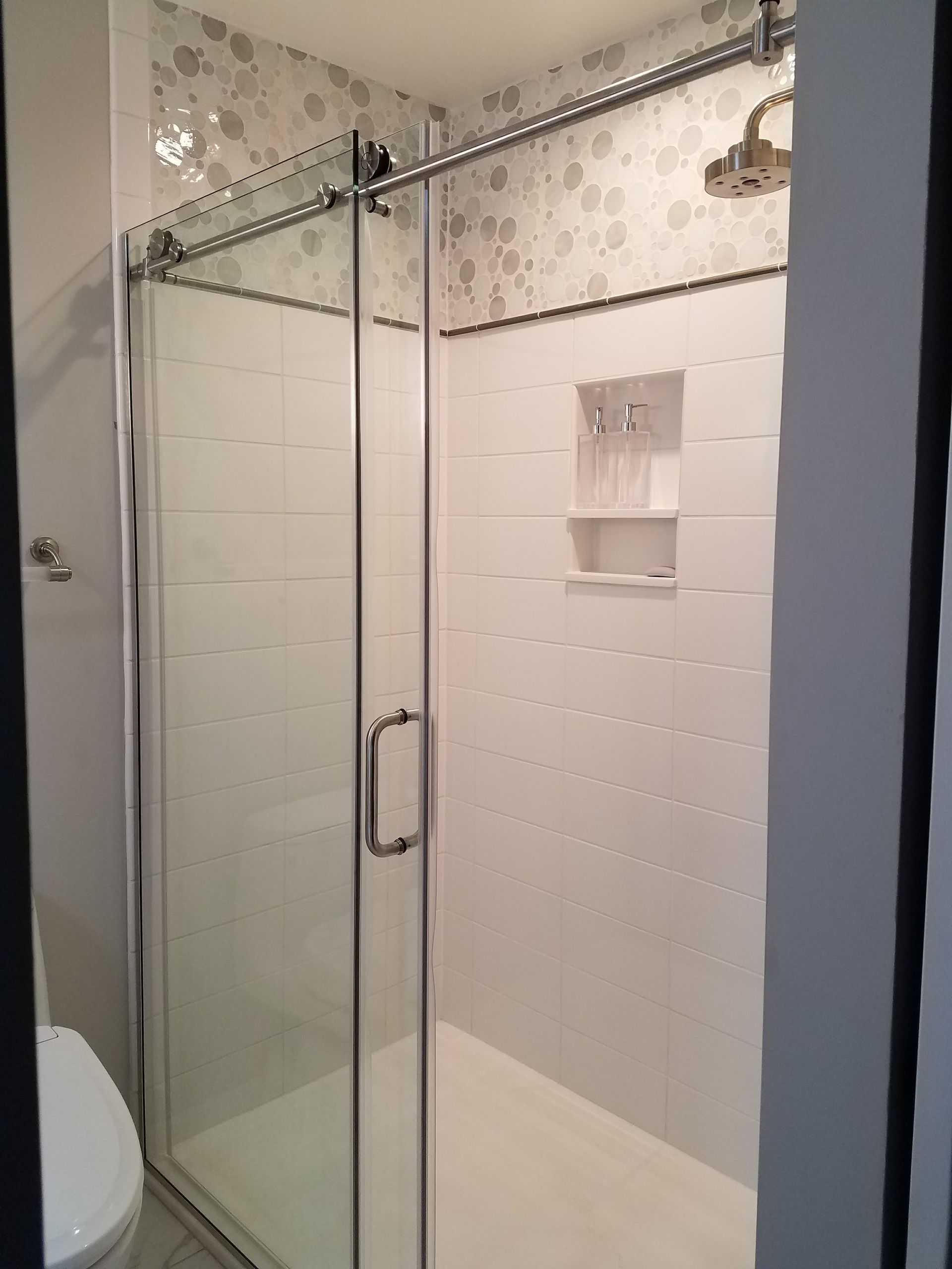 Glass shower with sliding door, white tile walls, and a built-in shelf.