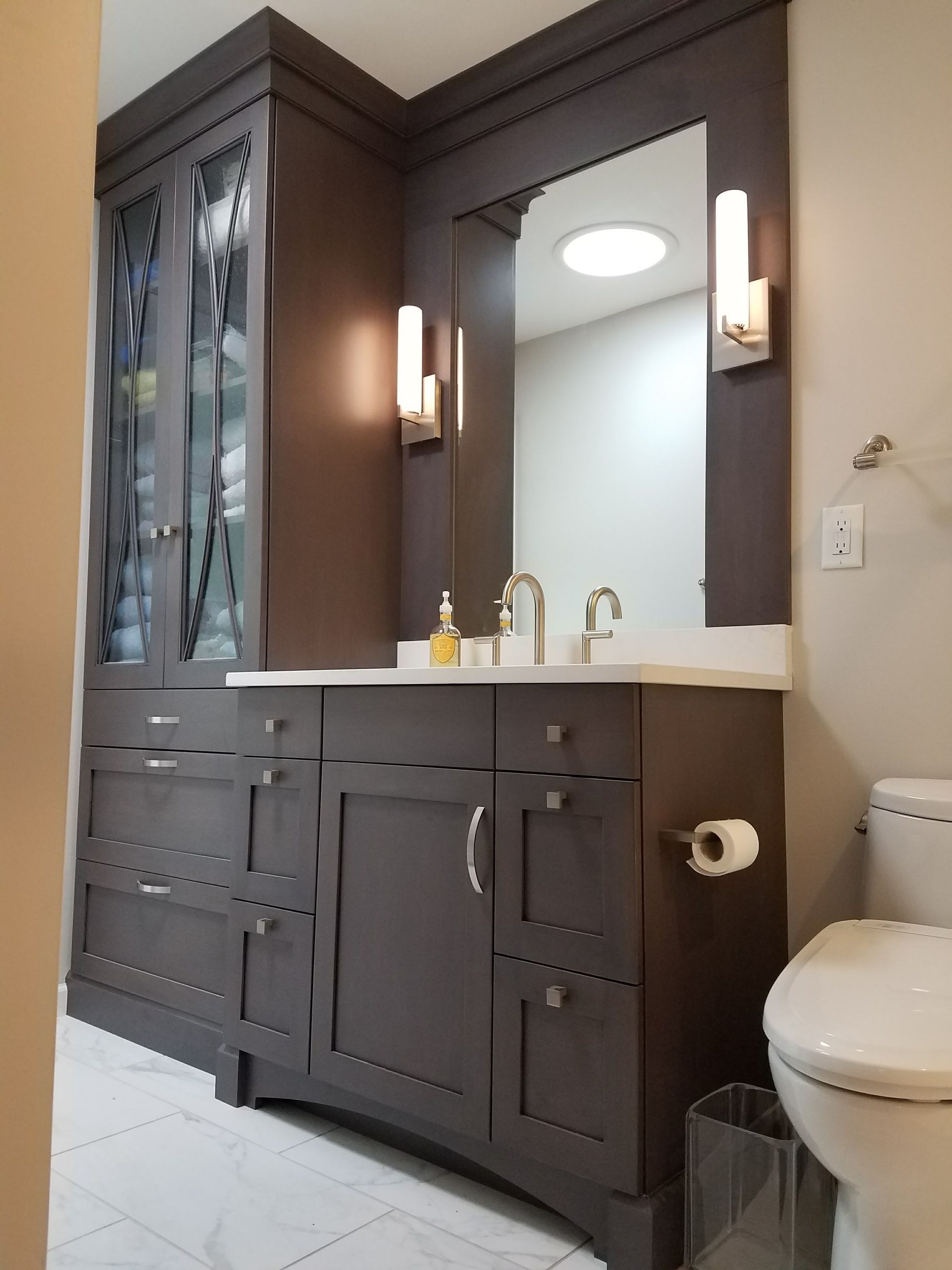 Dark gray bathroom vanity with mirror and storage cabinet, light walls, and a toilet.