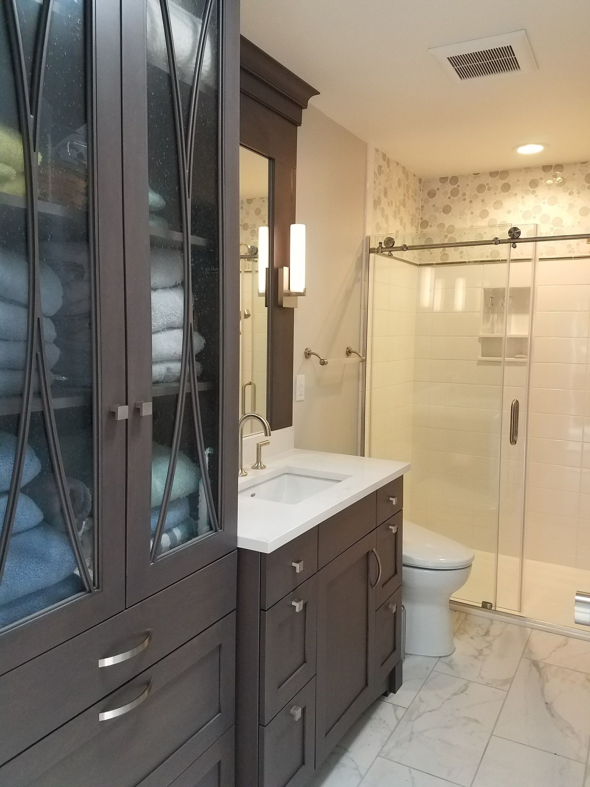 Bathroom with dark cabinets, a white sink, shower with sliding glass door, and stacked towels.
