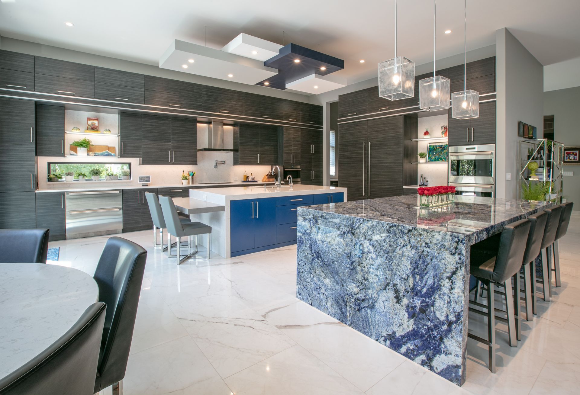 Modern kitchen with gray cabinets, two blue islands, and marble floors.