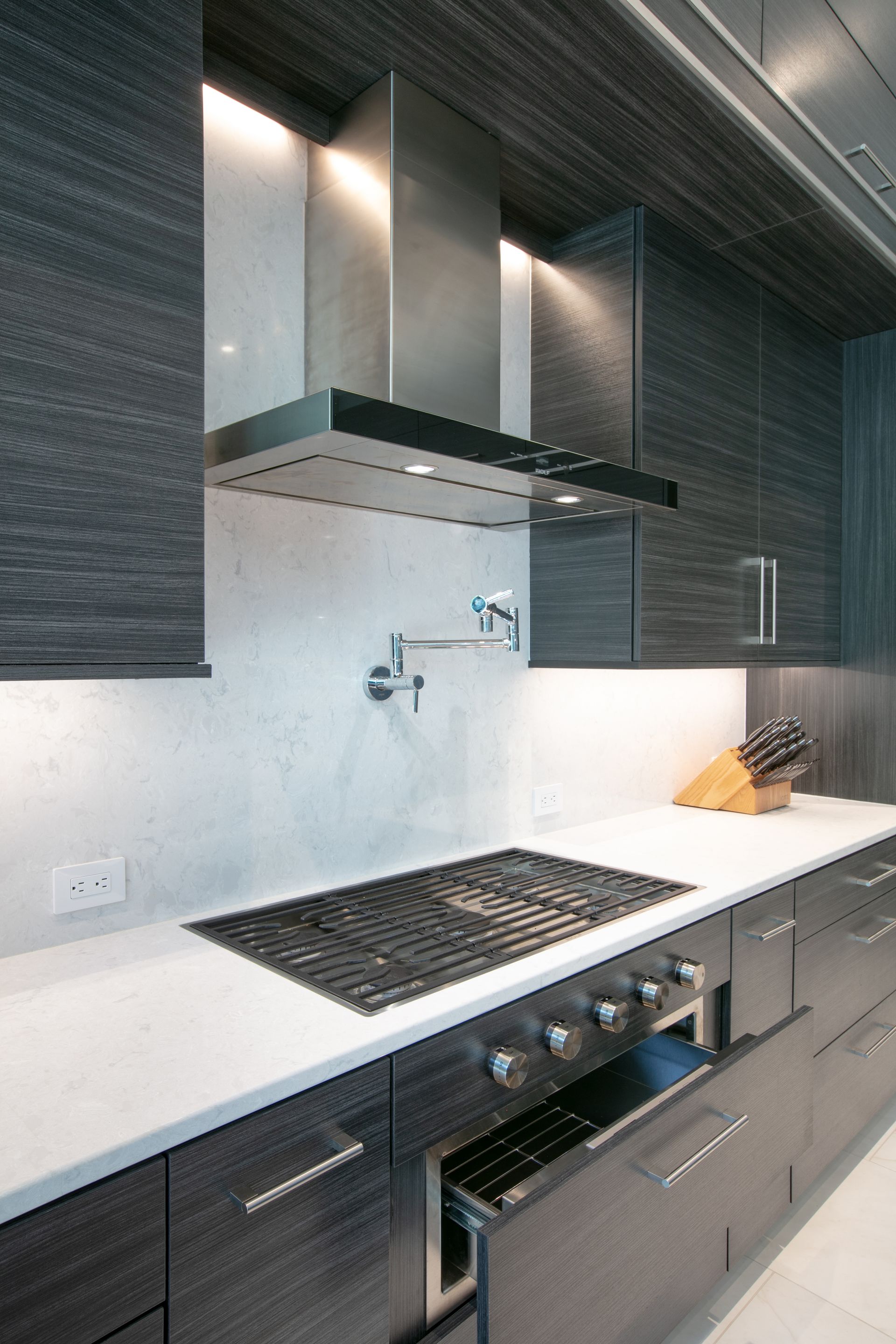 Modern kitchen with dark wood cabinets, white countertops, and a stainless steel range hood.
