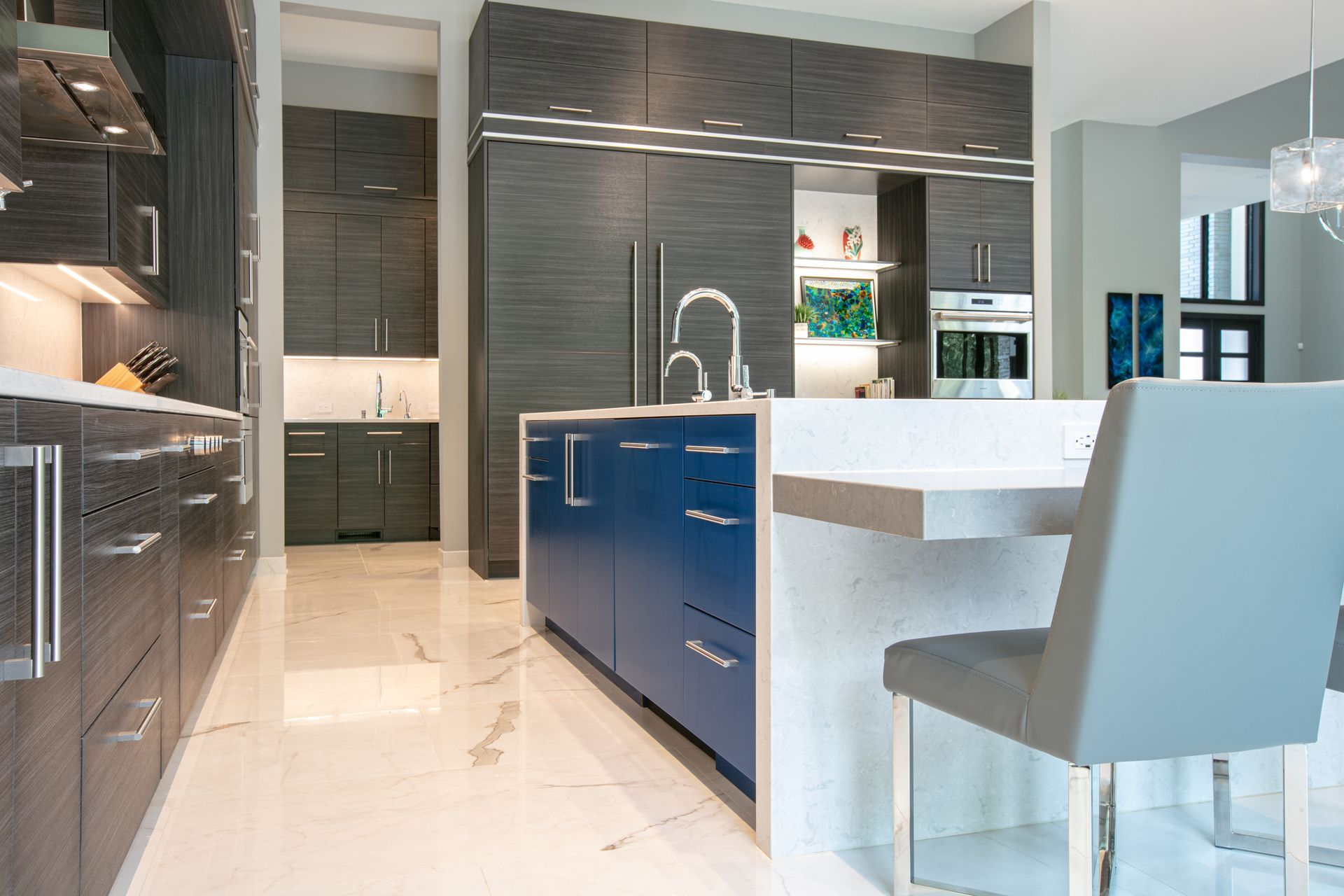 Modern kitchen with gray and blue cabinetry, white countertops, and marble flooring.