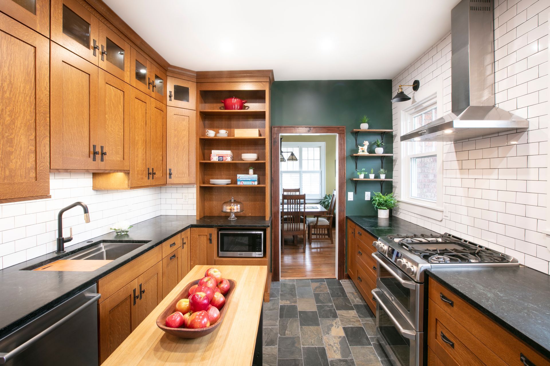 Wooden kitchen with black counters, white brick backsplash, and a wooden island with a fruit bowl.