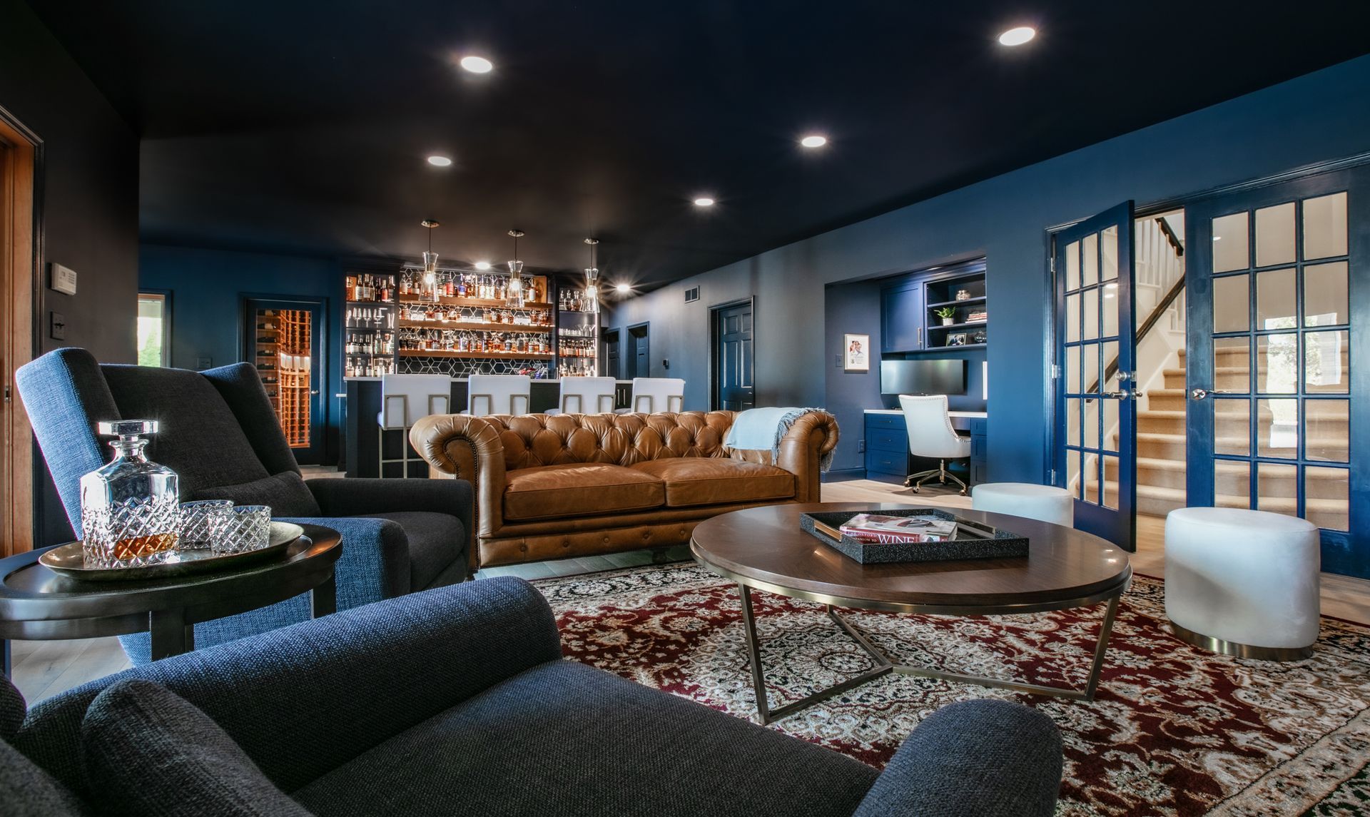 Upscale lounge with blue walls, a bar, leather sofa, and armchairs.