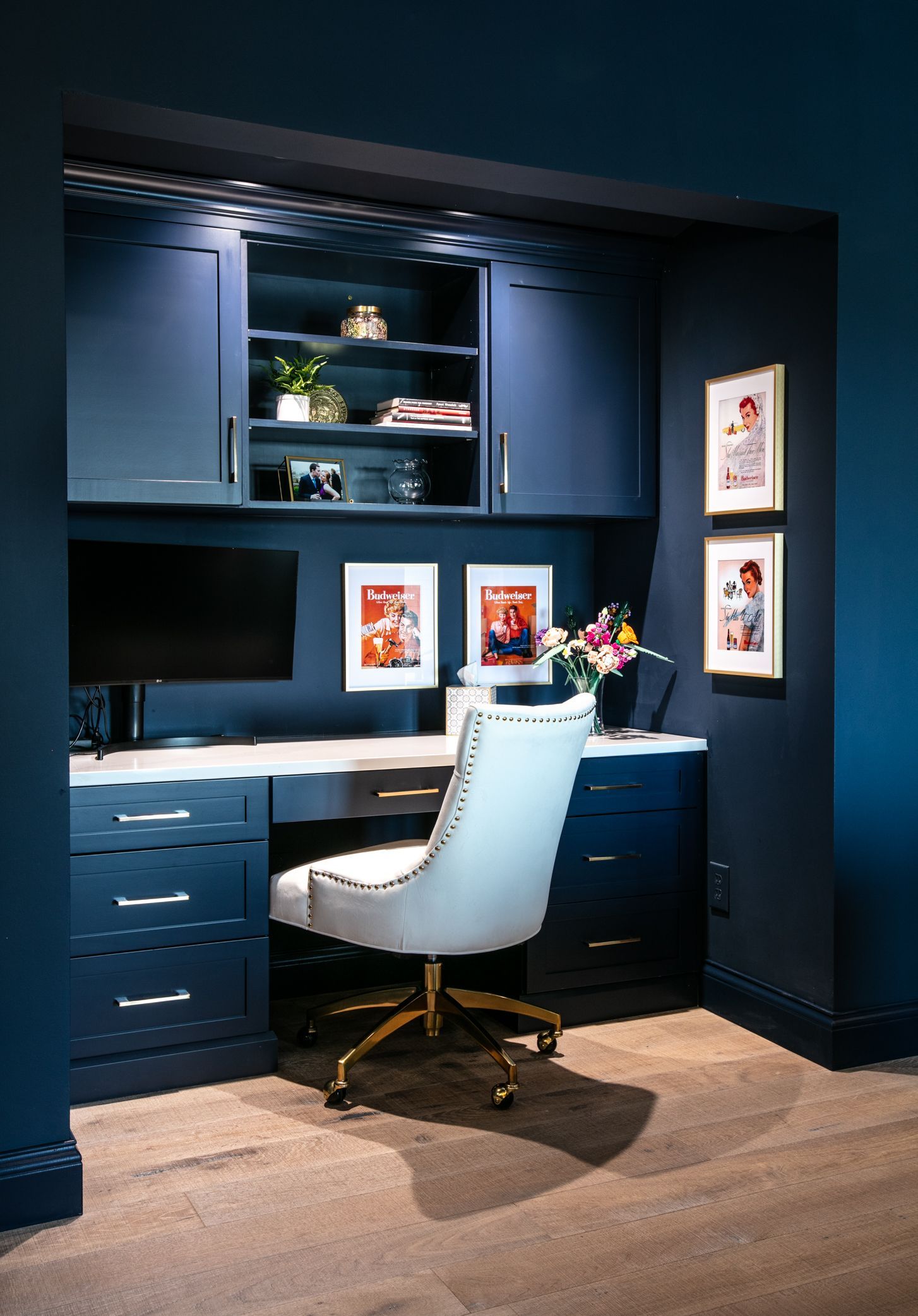 Built-in home office in navy blue with white desk, chair, and framed photos.