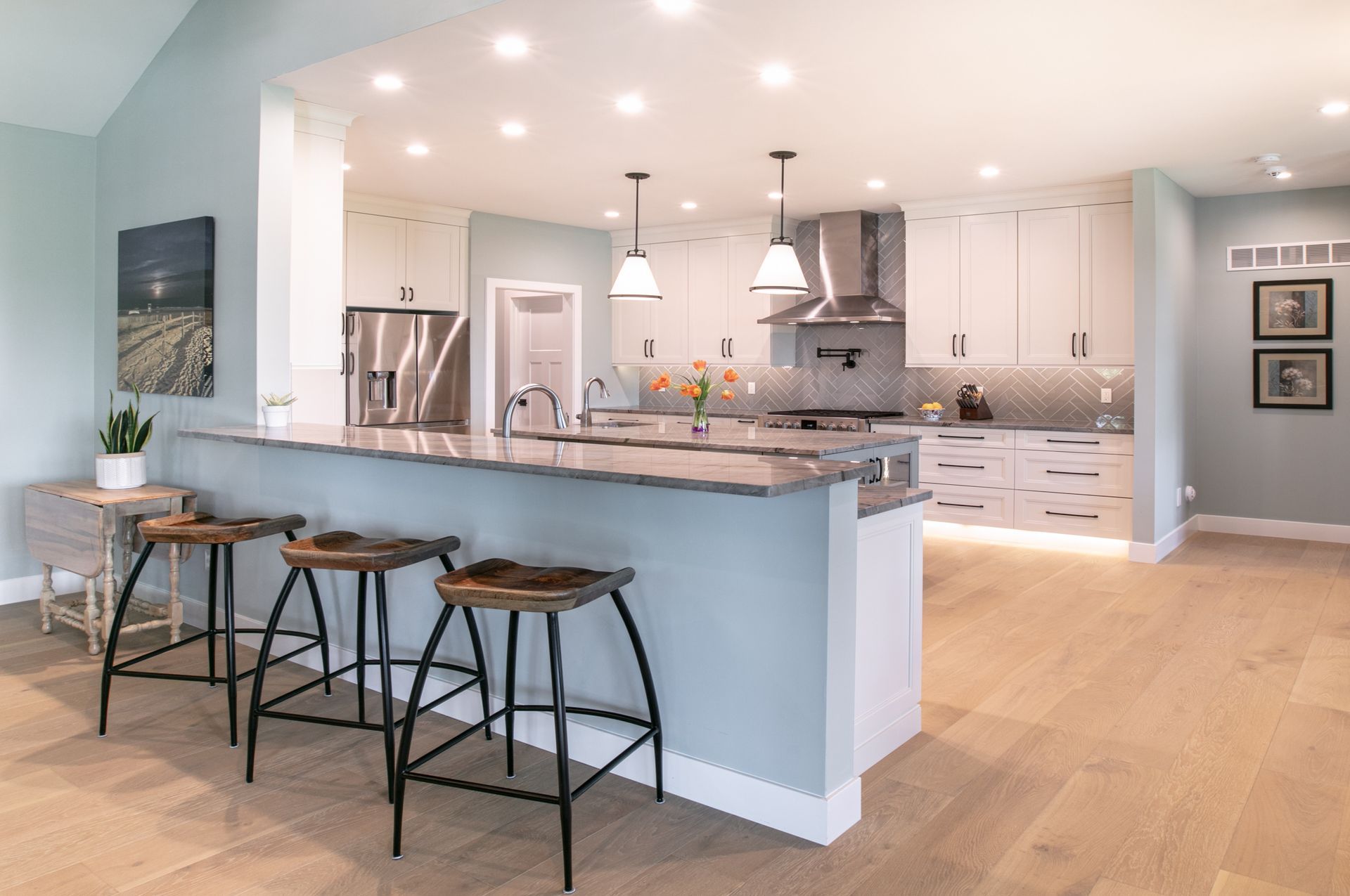 Modern kitchen with light blue walls, gray countertops, and wooden stools at a breakfast bar.