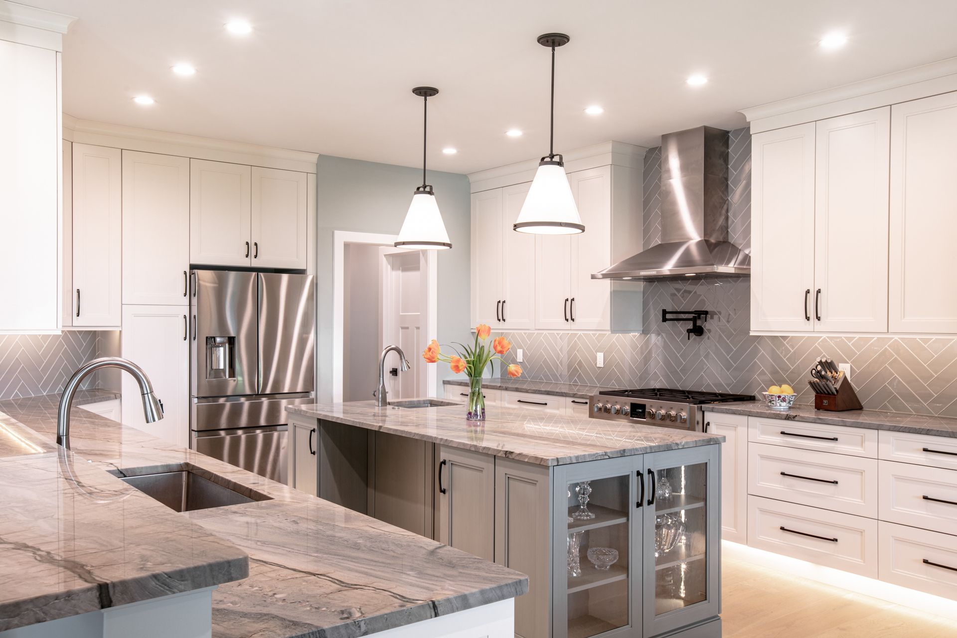 Modern kitchen with stainless steel appliances, light cabinets, gray island, and pendant lights.