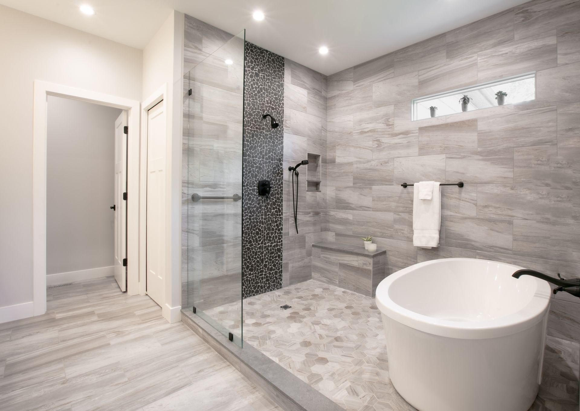 Modern bathroom with a walk-in shower, freestanding tub, and gray tile walls and floors.