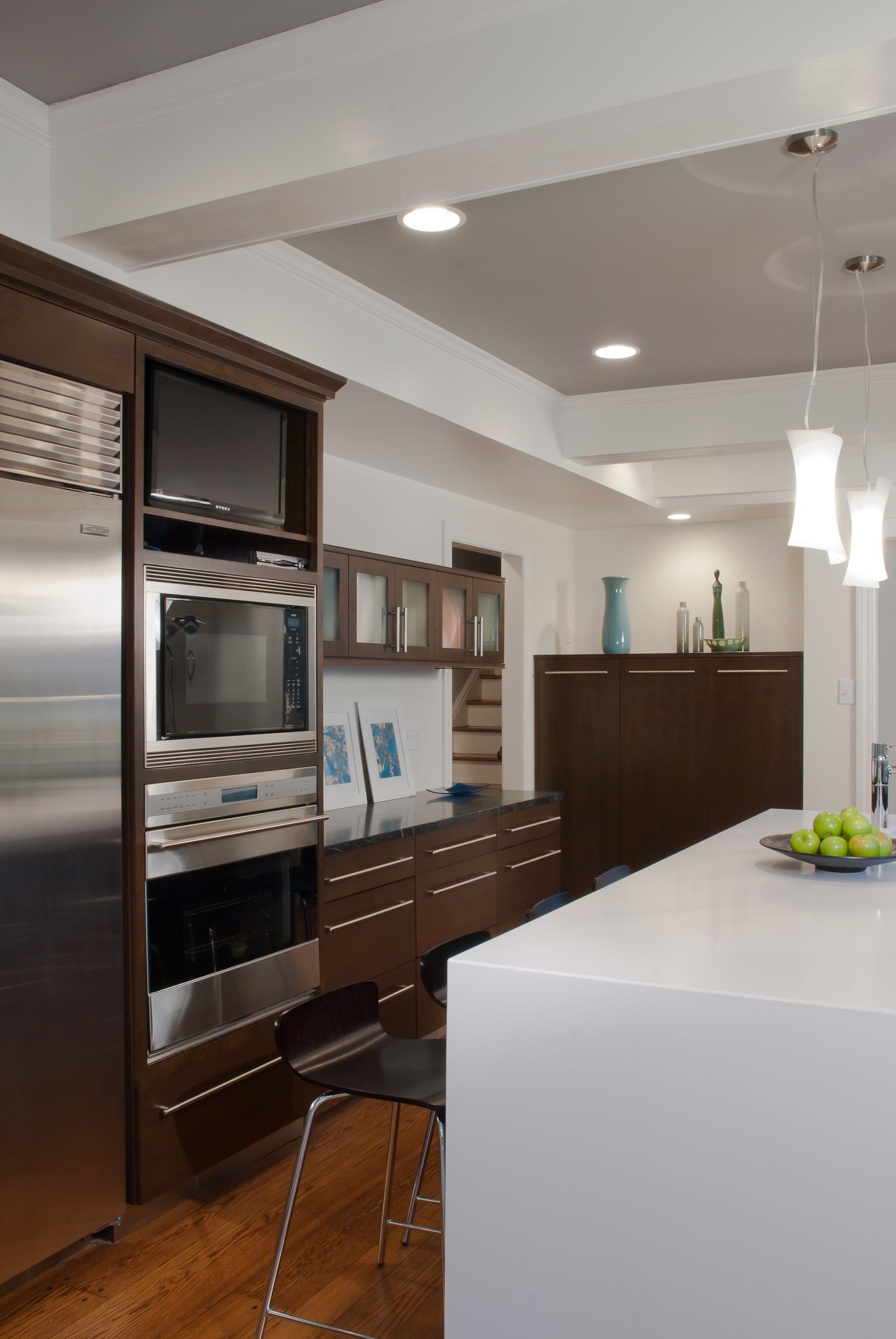 Modern kitchen with stainless steel appliances, dark wood cabinetry, and white countertops.