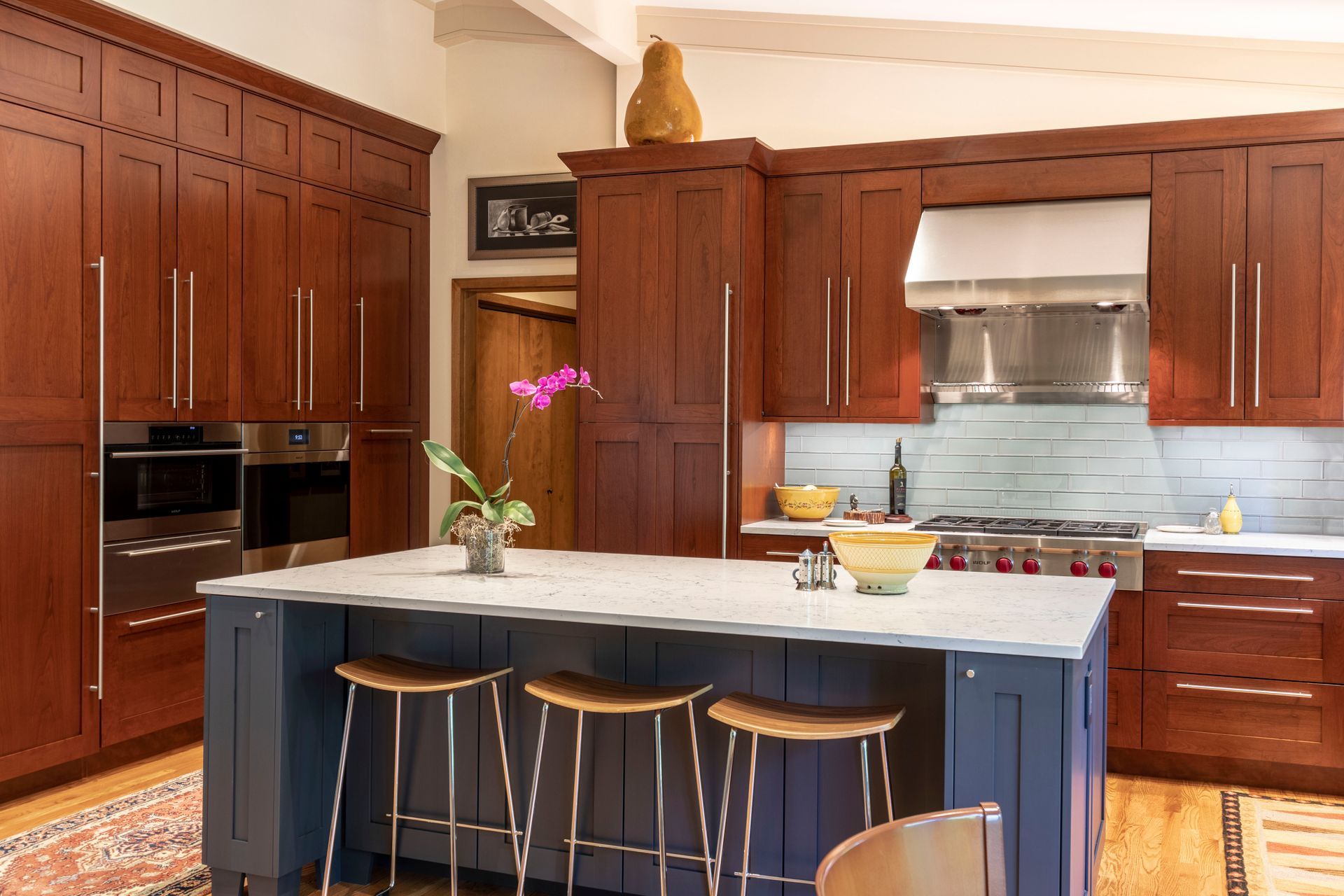 Kitchen with dark wood cabinets, blue island, stainless steel appliances and stools.
